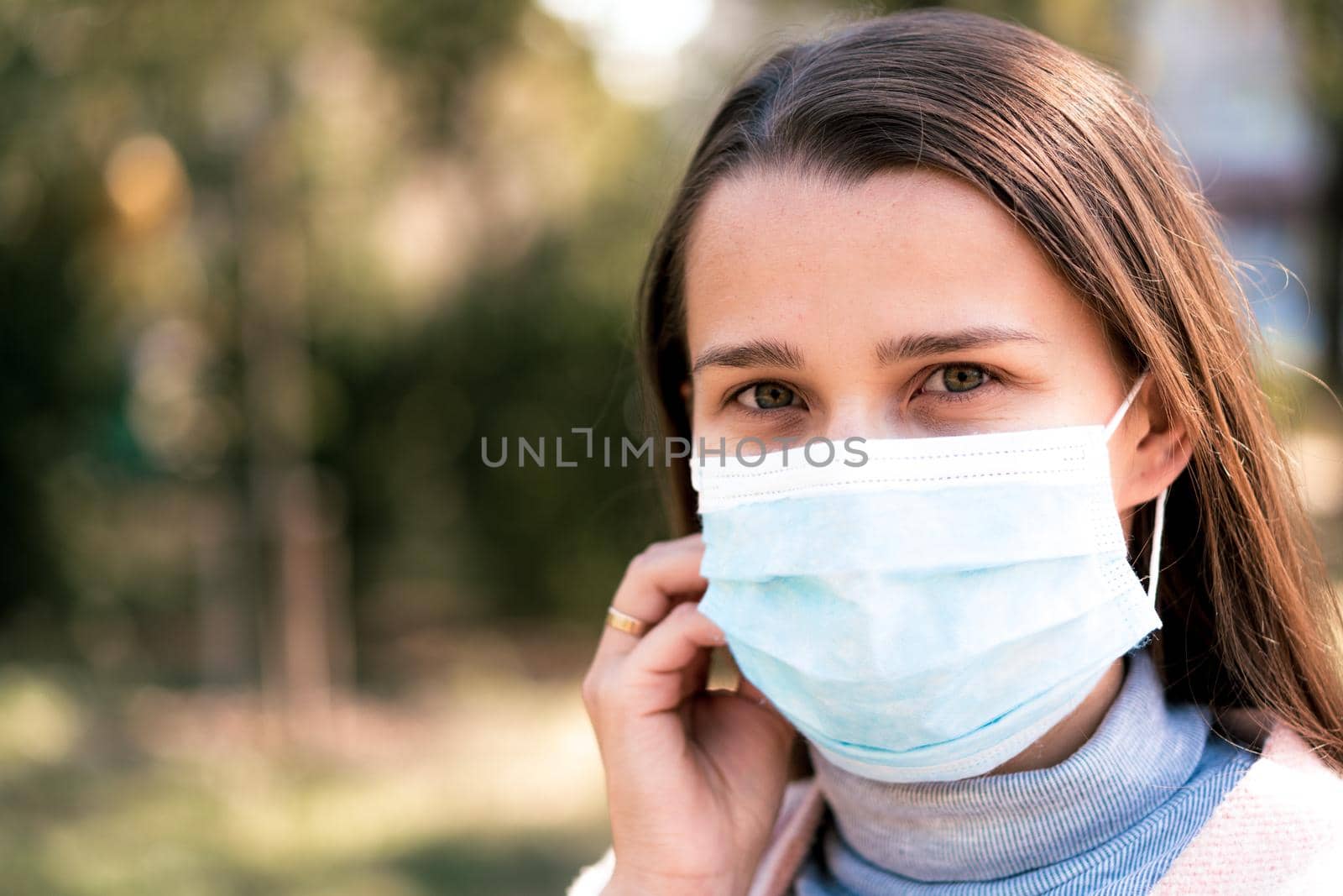 care, infants, spring, coronavirus and quarantine concept - Young cute long haired woman European Caucasian Slavic appearance put on blue medical protective mask in midday sunlight backlight in park