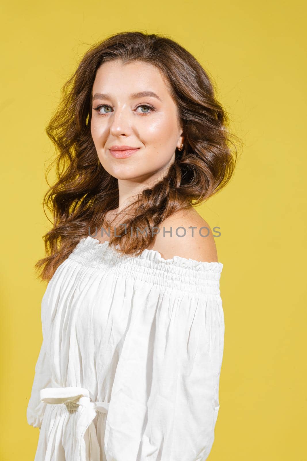 Beautiful bright woman in the studio on a yellow background in a white light dress smiling happy,