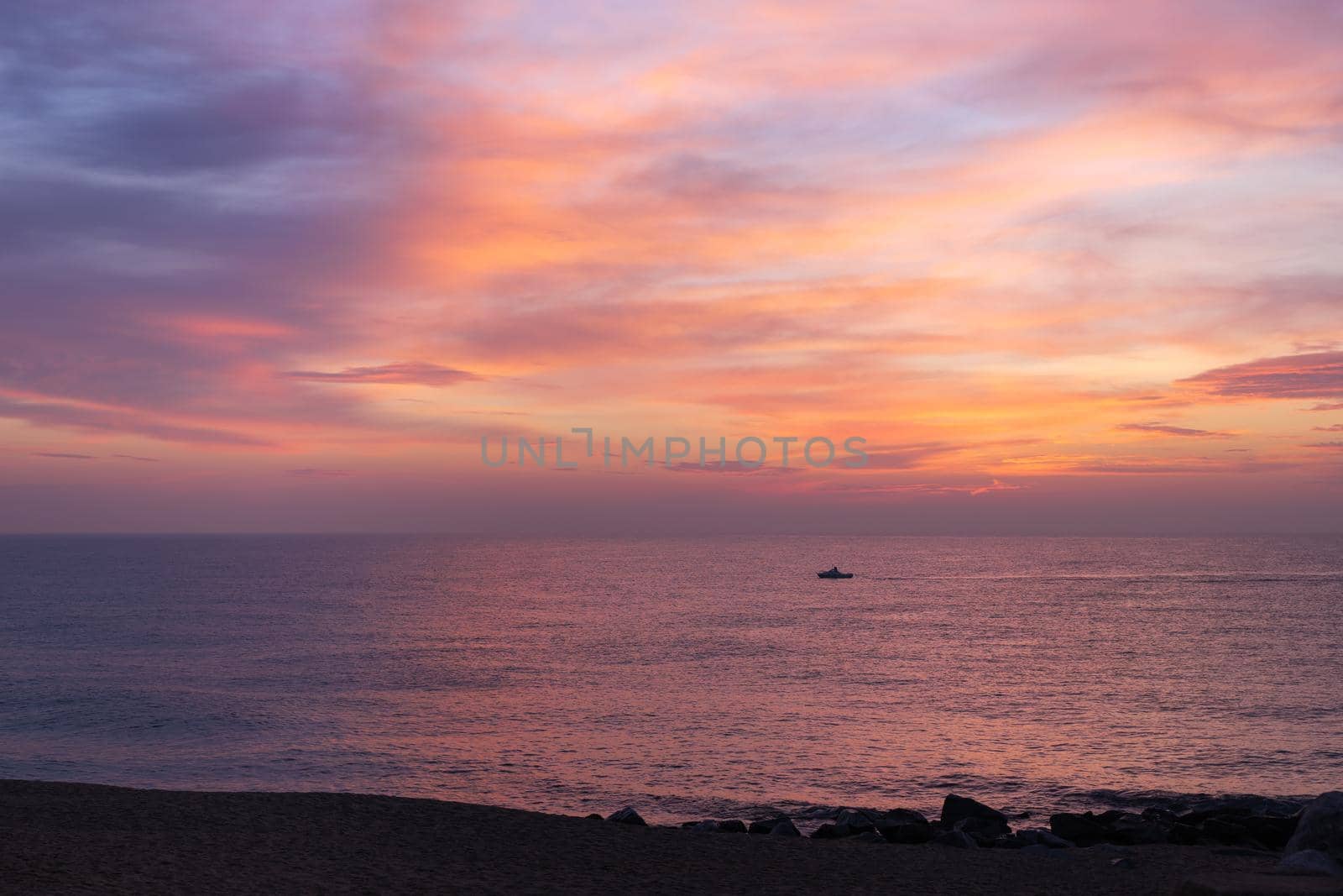 Morning pink sky reflected in the sea. A small lonely fisherman boat silhouette sailing during the sunrise. Soft color sunset on ocean coast, beautiful seascape