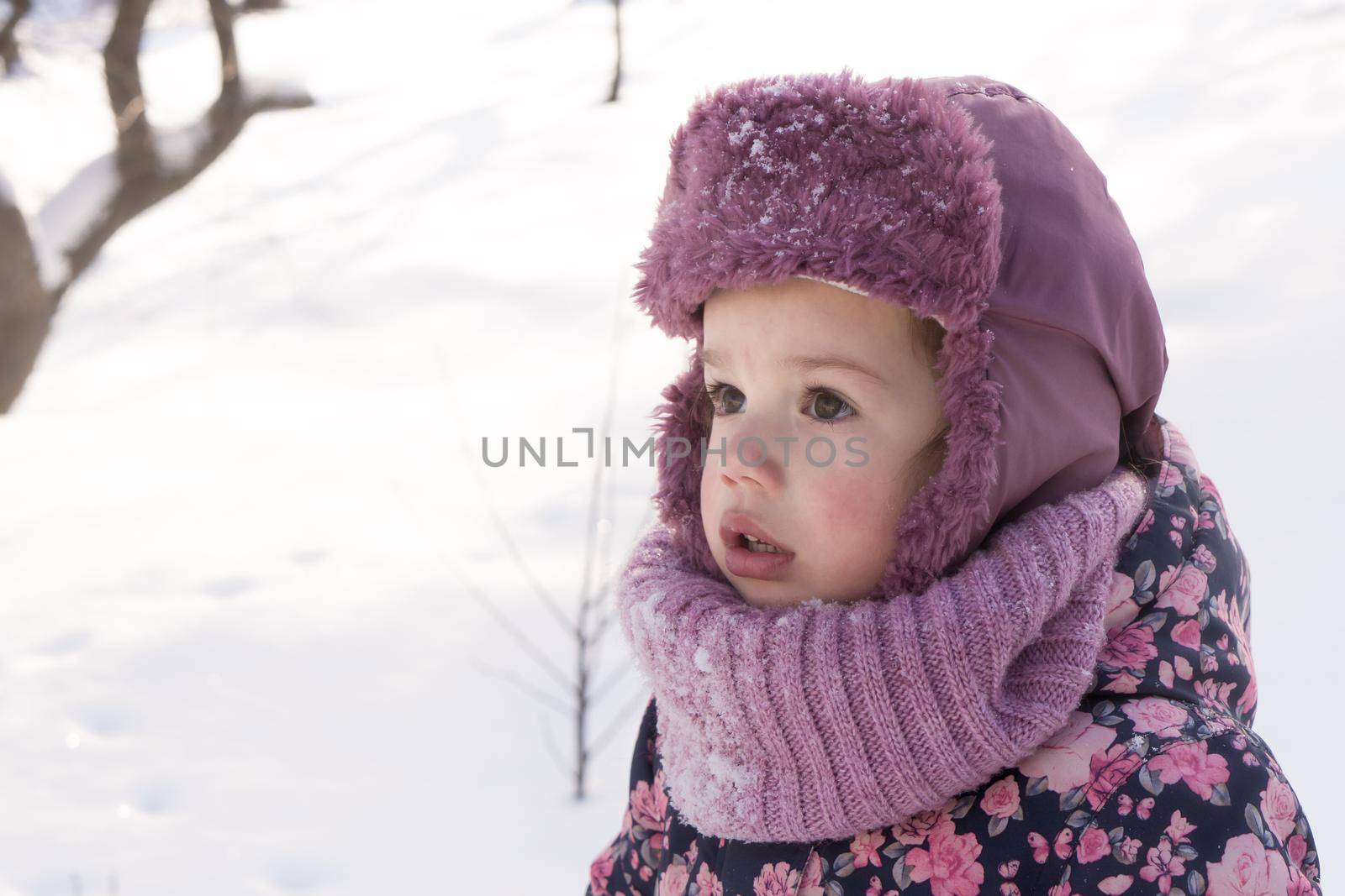 Winter, family, childhood concepts - close-up portrait authentic little preschool minor girl in pink look around in snowy frosty weather. surprised mysterious worried kid face outdoors. copy space.