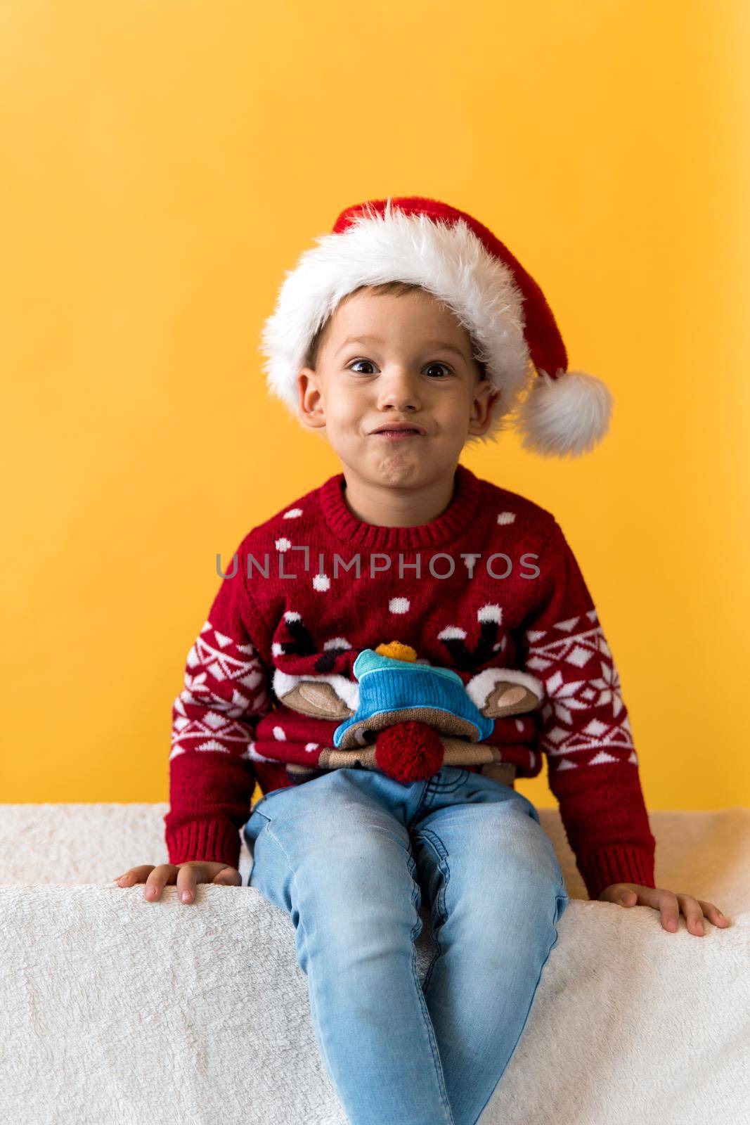 Portrait of happy smiling positive joyful positive preschool little boy in red warm santa hat showing thumb up on orange, yellow background. Winter, holiday, celebration, Christmas, New Year copy space.