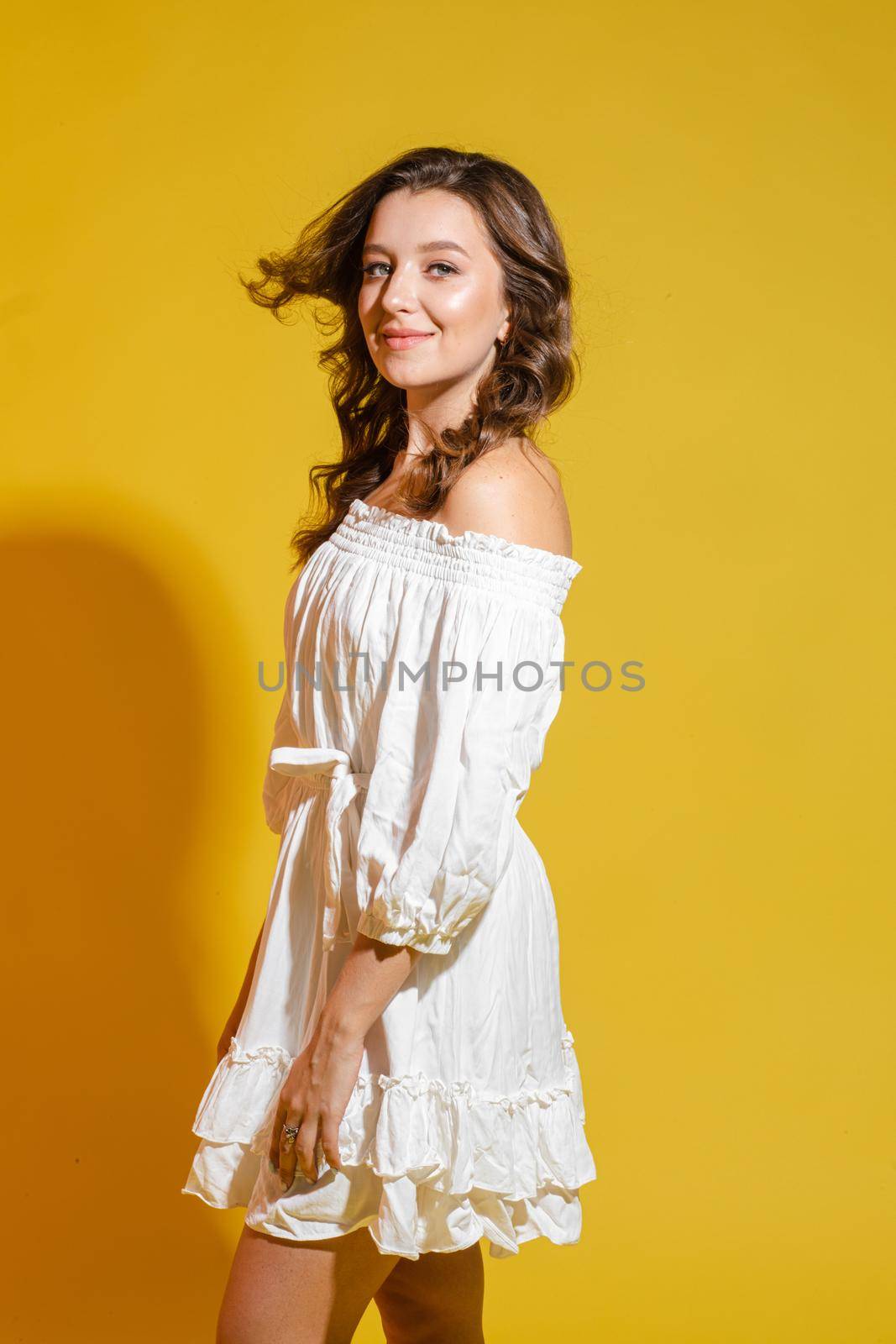 Beautiful bright woman in the studio on a yellow background in a white light dress smiling happy by StudioLucky