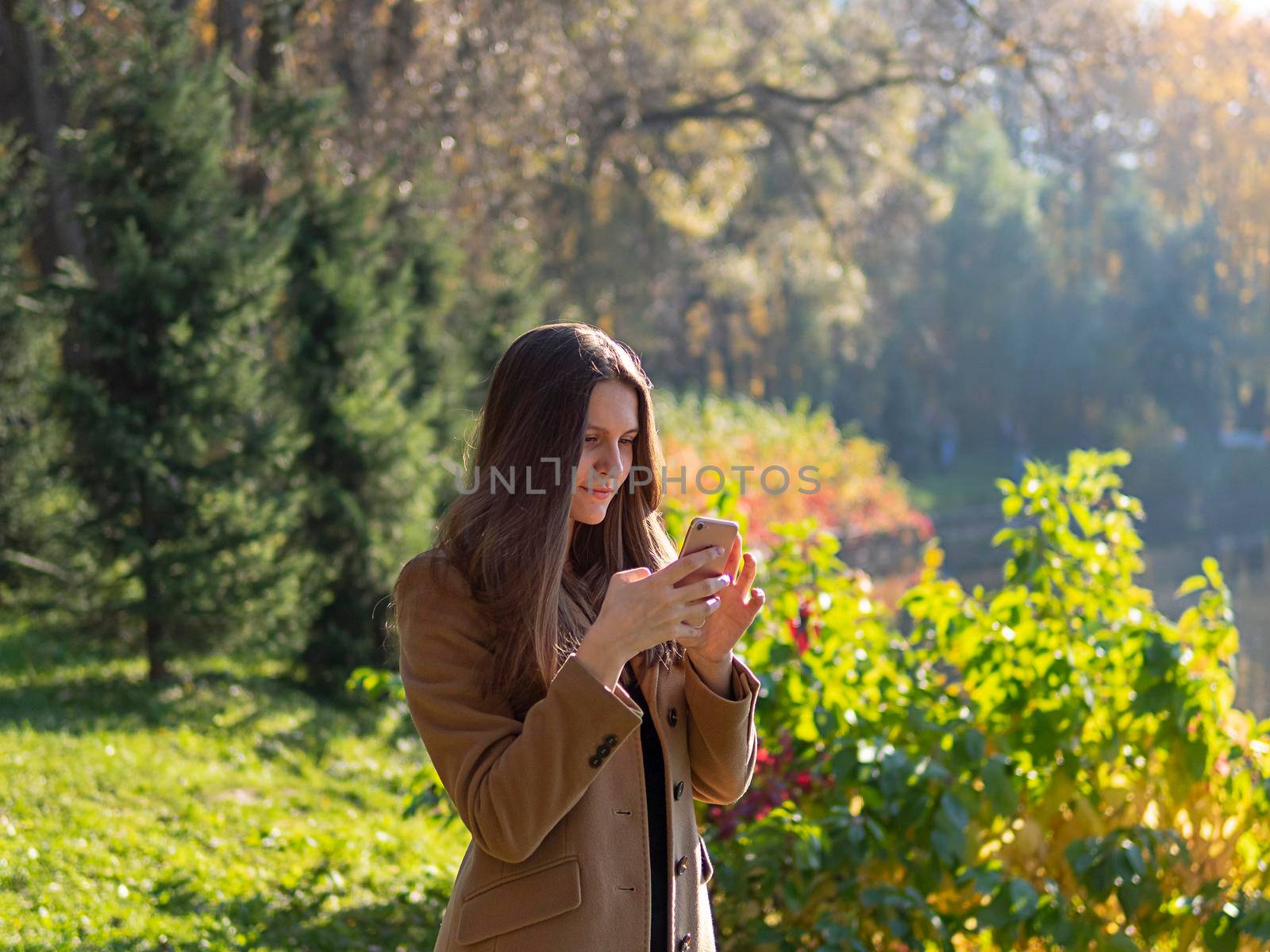 Beautiful teen girl in the Park, holding smartphone and chatting online on Internet. Young woman with long hair.