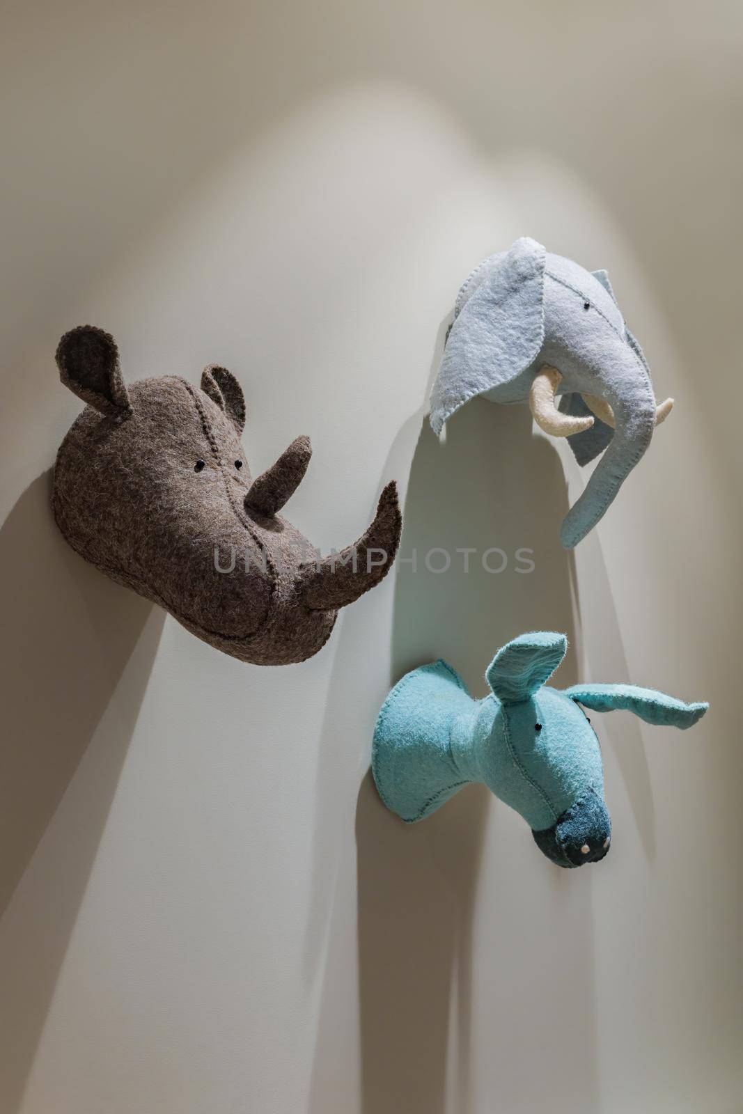 Felted animals toys hanging on the wall. Heads of donkey, rhinoceros and elephant on gray wall. Emulation of trophies from hunting in the children's room
