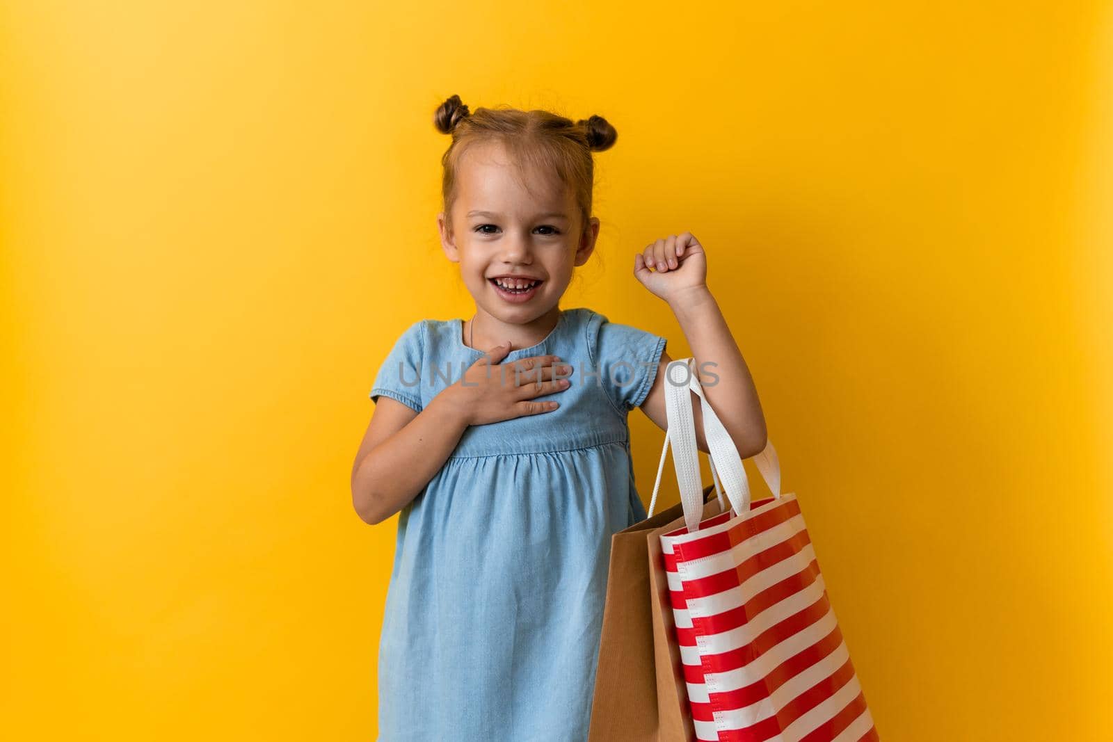 Portrait Caucasian Beautiful Happy Little Preschool Girl Smiling Cheerful And Holding Cardboard Bags Isolated On Orange Yellow Studio background. Happiness, Consumerism, Sale People shopping Concept.