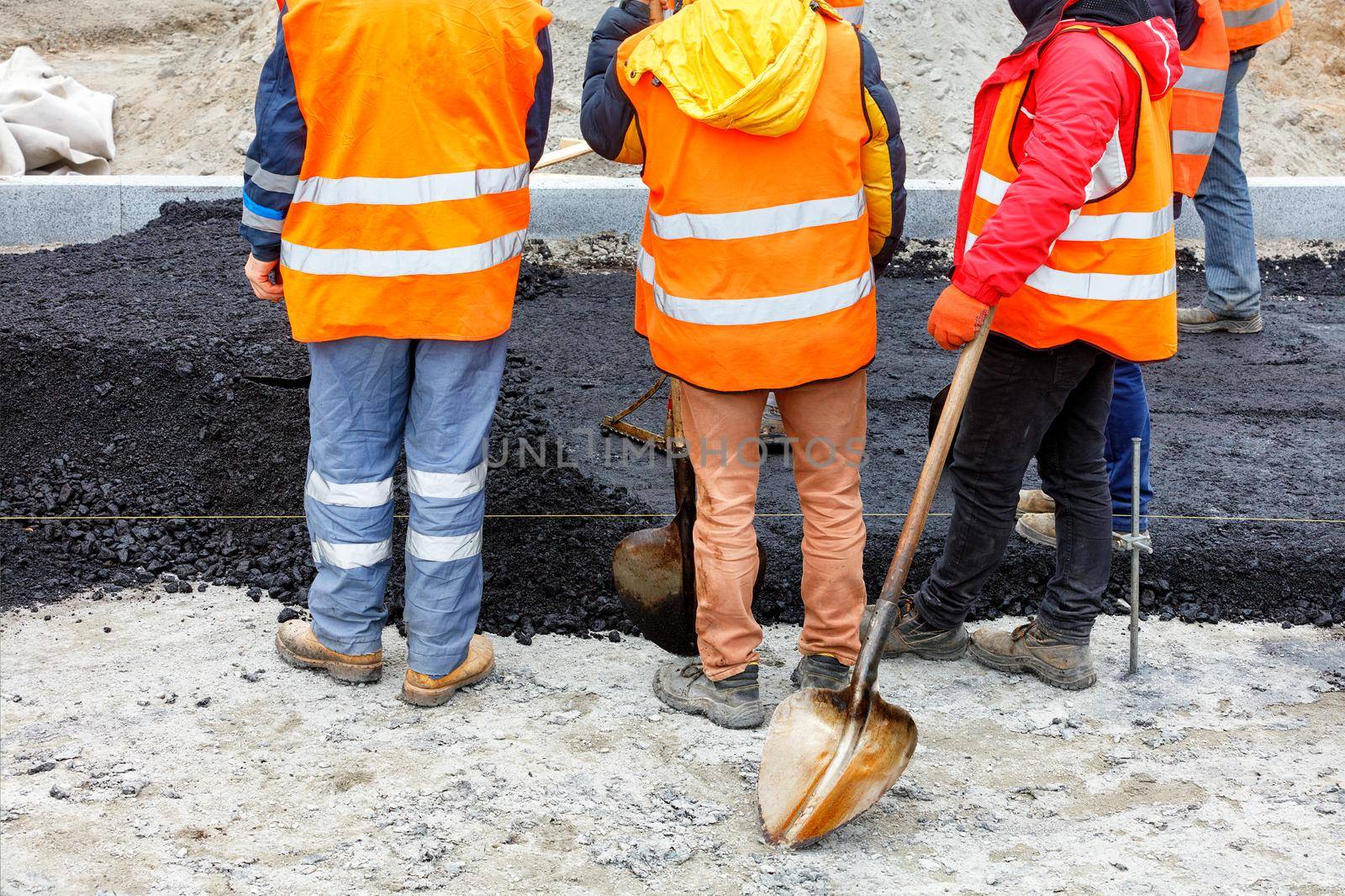 A working group of road workers in orange overalls got together to discuss a work plan for paving the section of the road with fresh hot asphalt. Copy space.