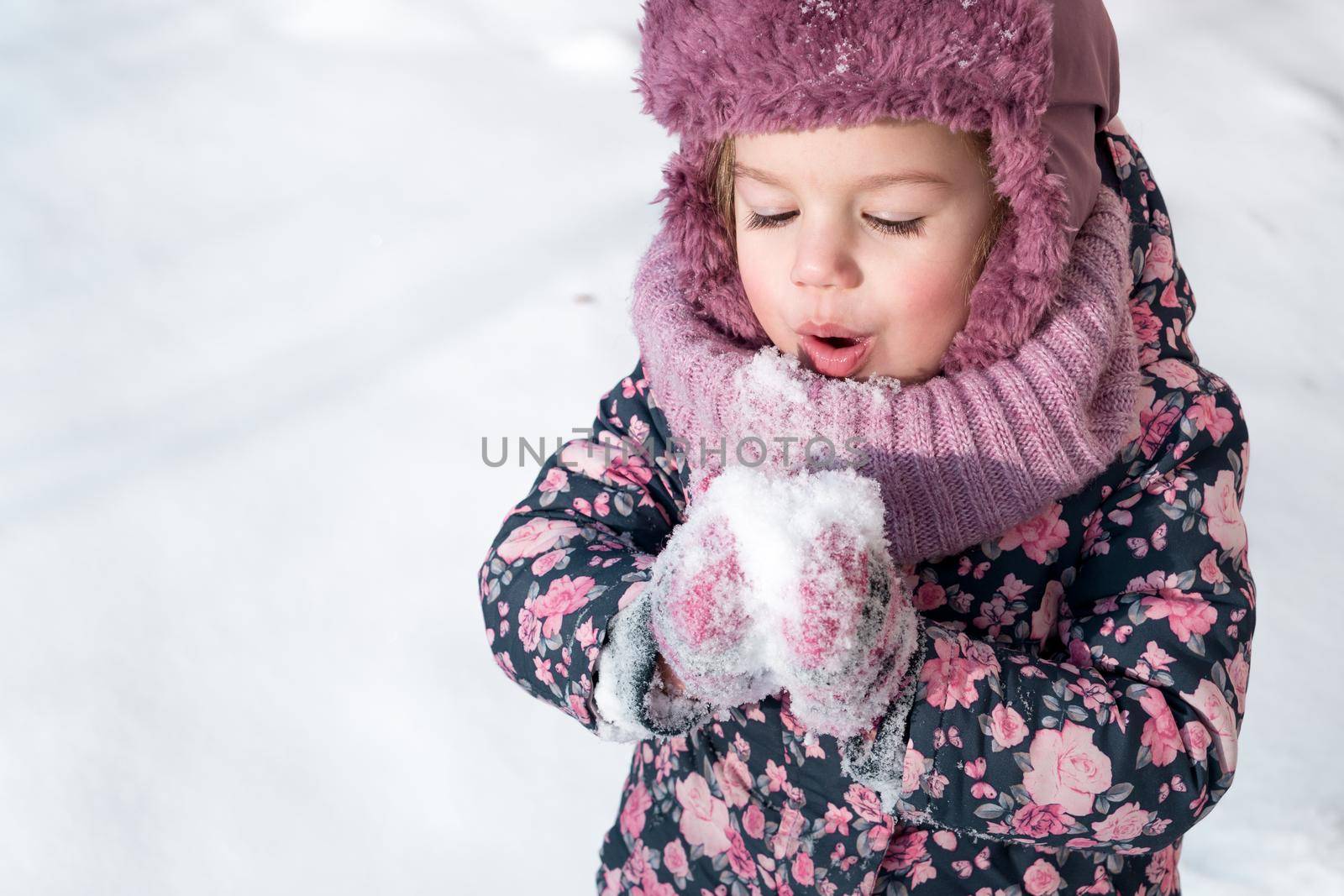 Winter, games, family, childhood concepts - close-up portrait authentic little preschool minor girl in pink hat warm clothes have fun smiles in cold frosty weather day. Funny kid blow on white snow by mytrykau