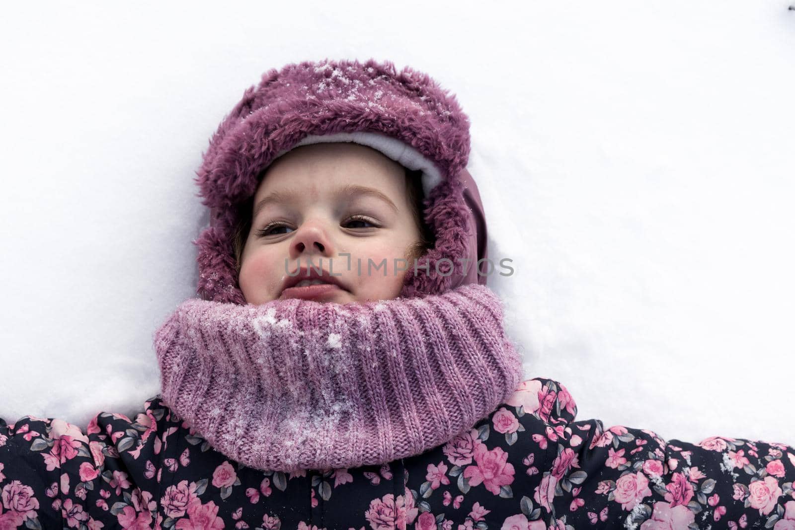 Winter, family, childhood concepts - close-up portrait authentic little preschool minor girl in pink clothes smile laugh closing eyes laying on snow in frosty weather day outdoors. Funny kid face by mytrykau
