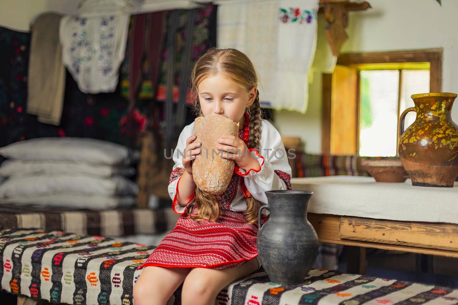 girl in Ukrainian national costume eats bread sitting on a bench in the house