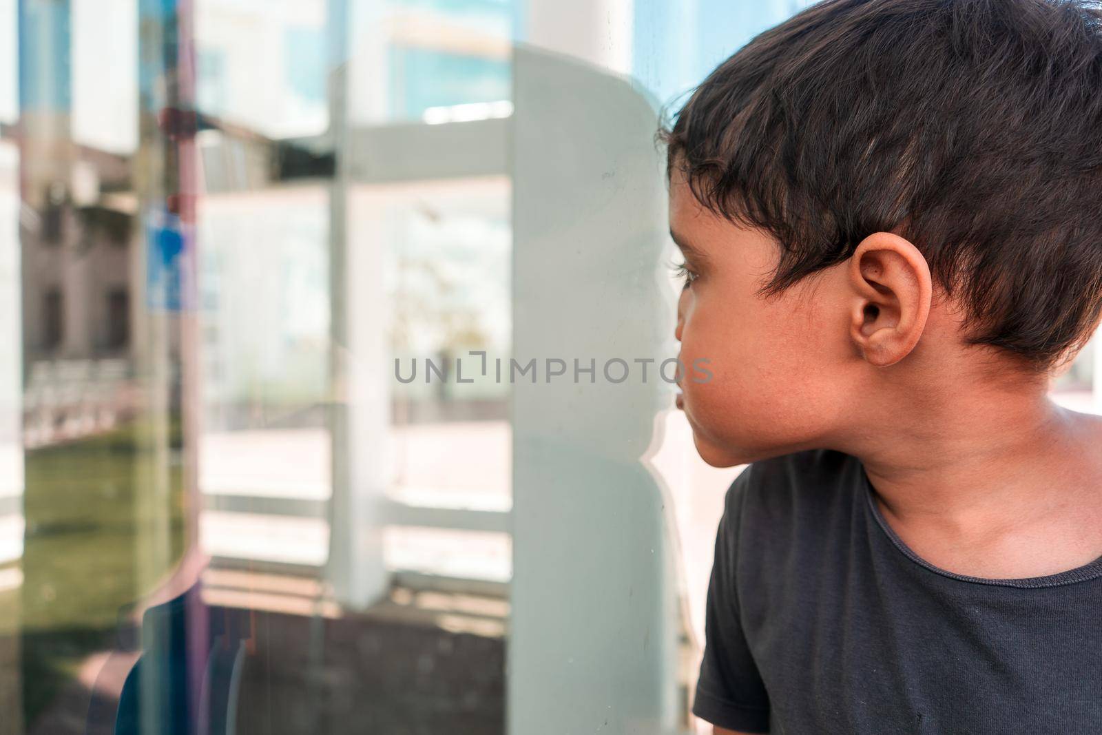Latino boy pressing his face against glass outdoors. Concept of self discovery in childhood.