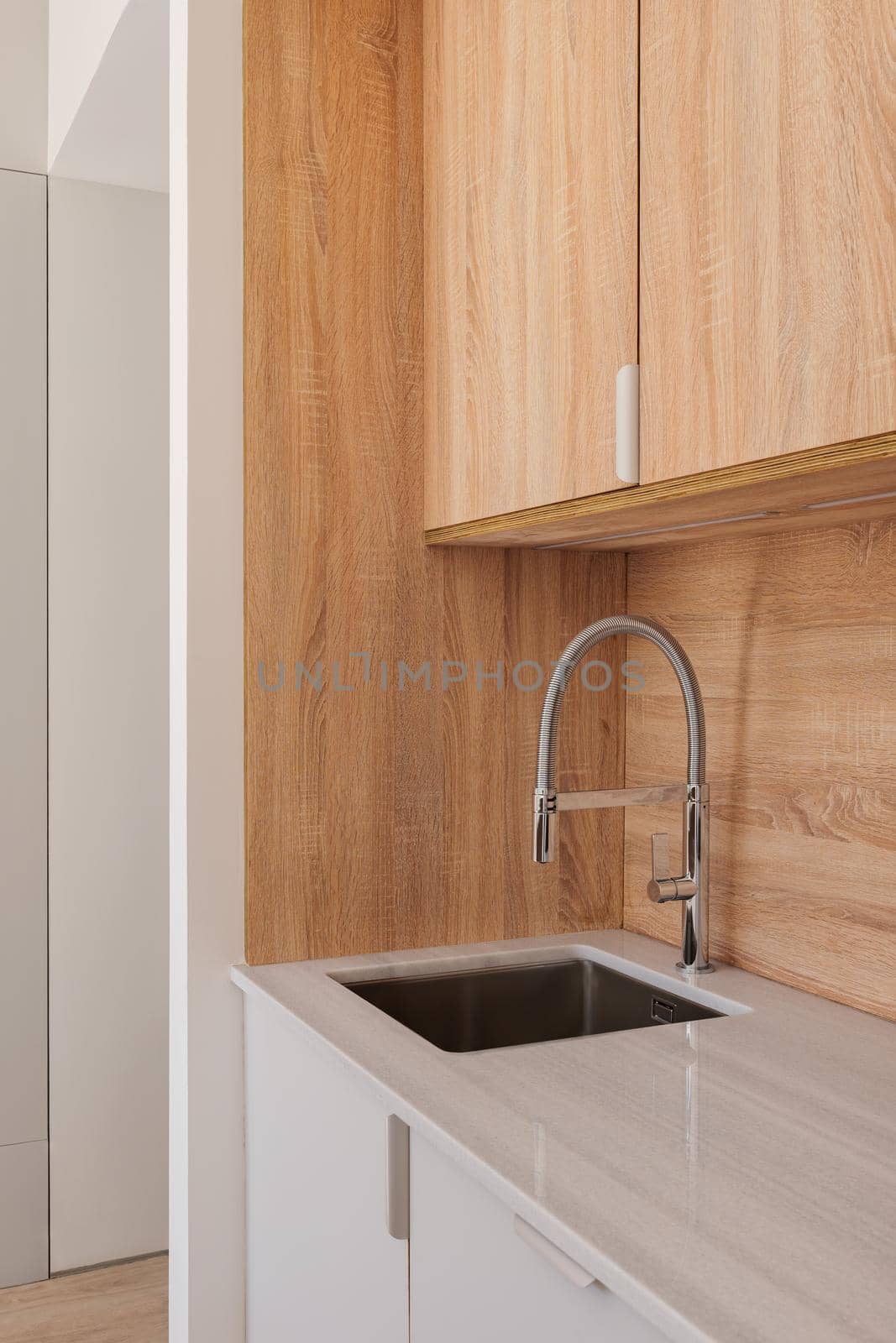 Modern faucet and sink in elegant kitchen with wooden cabinets. Minimalist style interior in refurbished apartment