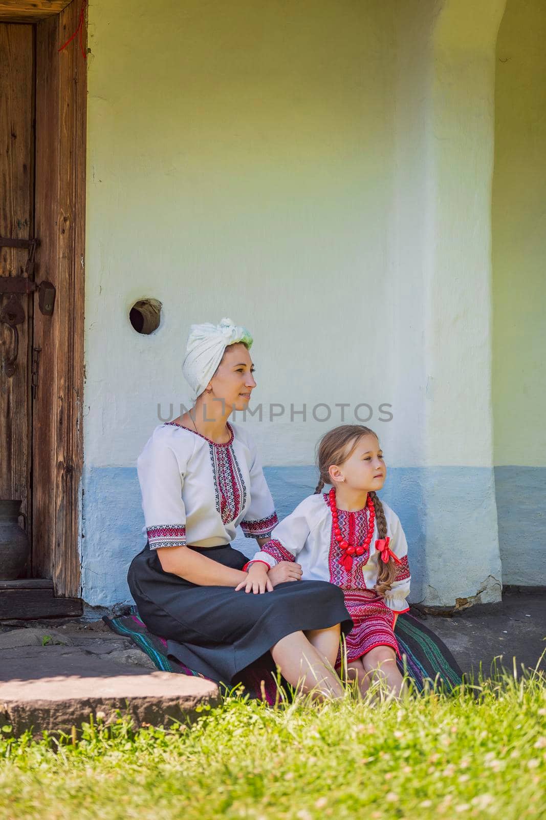 mother and daughter in Ukrainian national costumes are sitting near the house by zokov
