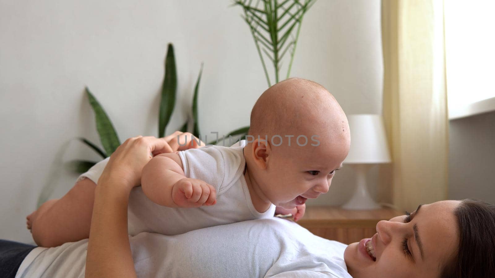 Authentic Young Caucasian Woman Holding Newborn Baby. Mom And Child On Bed. Close-up Portrait of Smiling Family With Infant On Hands. Happy Marriage Couple On Background. Childhood, Parenthood Concept by mytrykau
