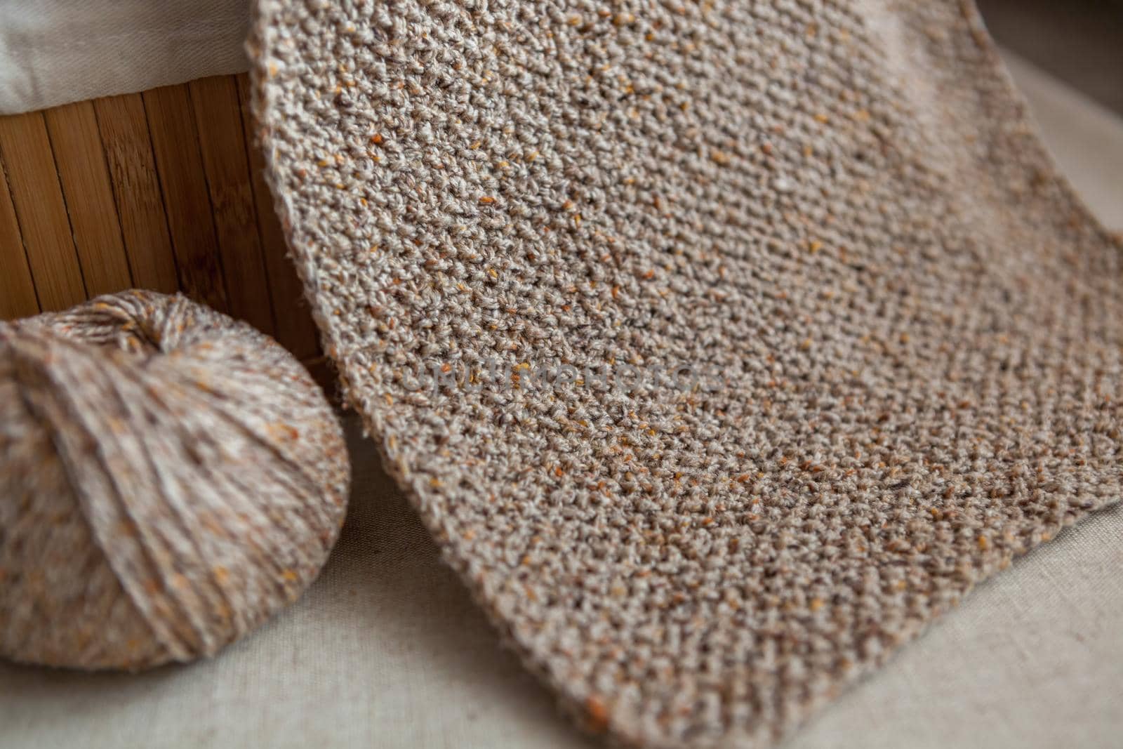 Handmade wool scarf of sand color and yarn ball. Close-up of knitted texture. Selective focus