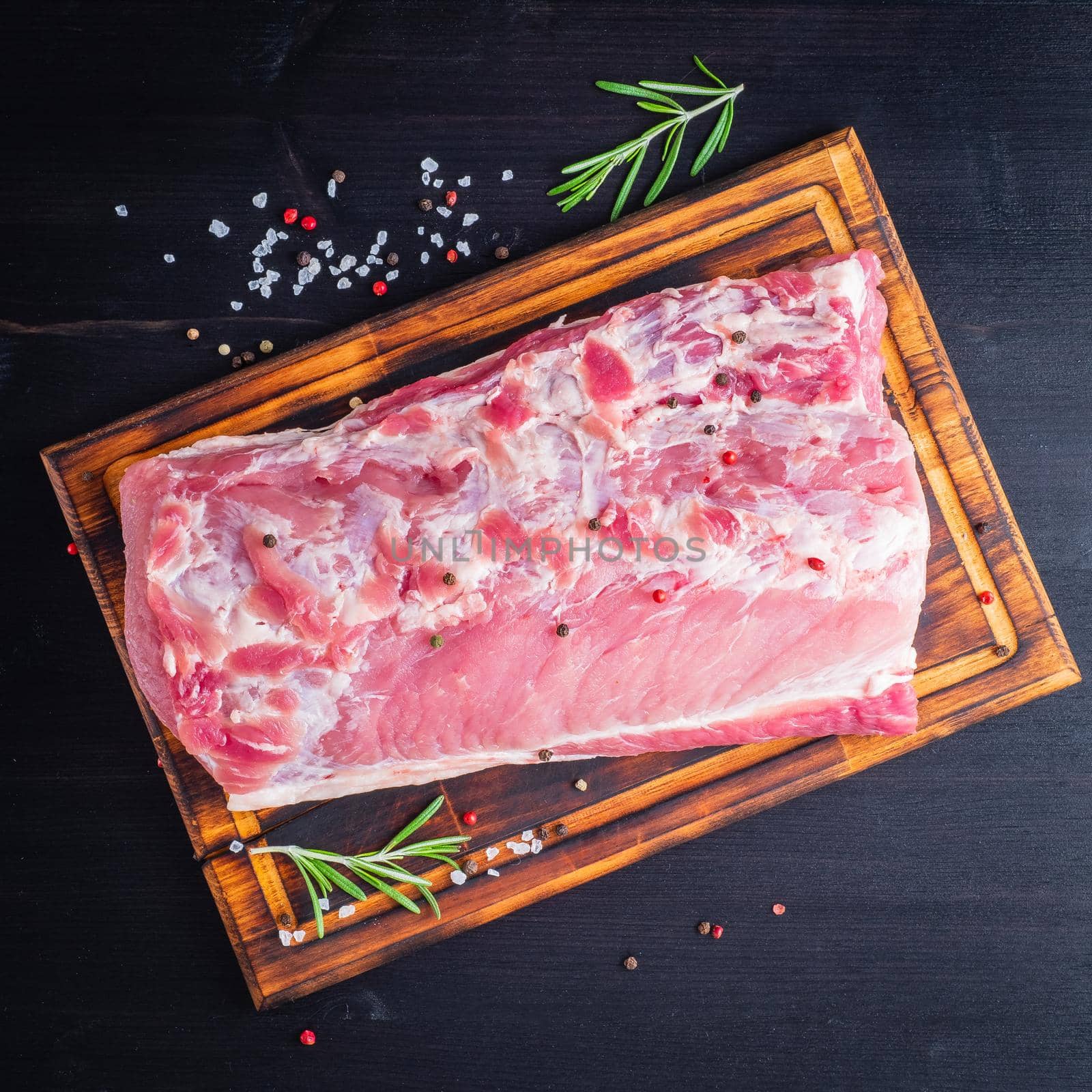 Big whole piece of pork meat with seasoning on chopping board on dark by NataBene
