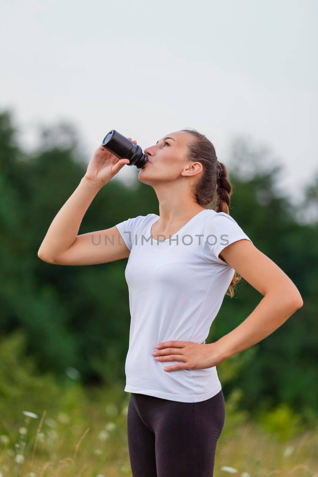 woman drinking water from a plastic bottle on the background of nature