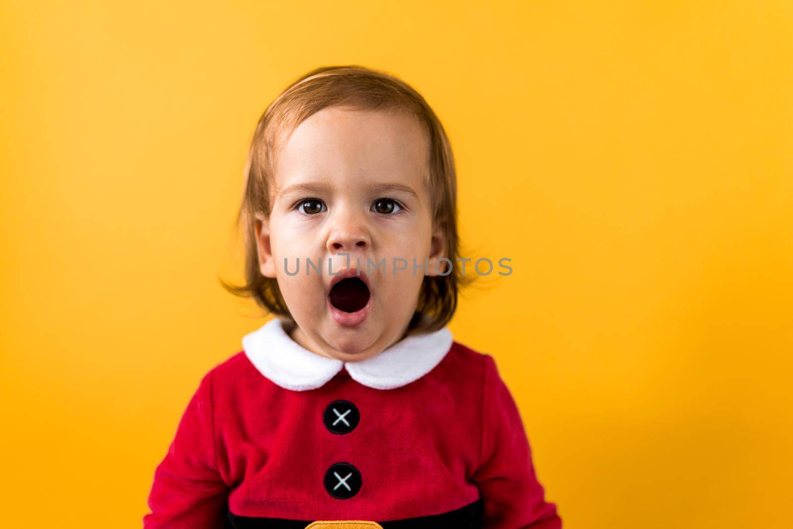 Portraite Emotion Cute Happy Cheerful Chubby Baby Girl in Santa Suit Yawns As If Singing At Orange Background. Child Christmas Scene Celebrating Birthday. Kid Have Fun Spend New Year Time Copy Space.
