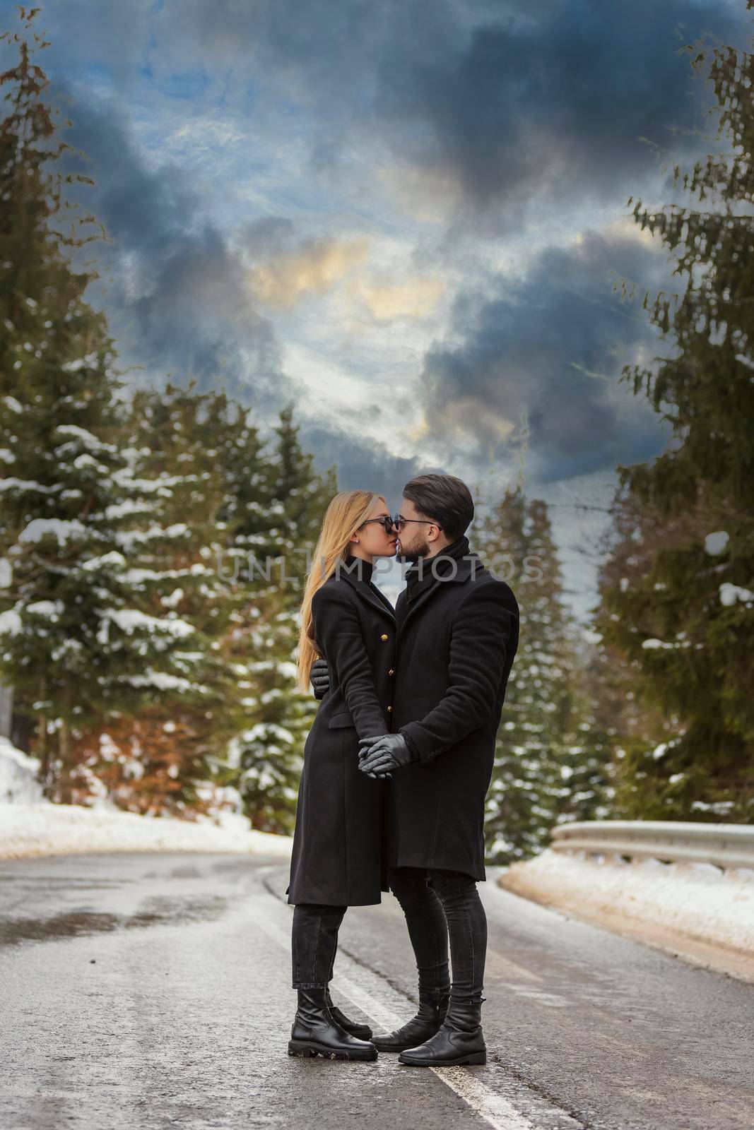 couple kissing against the backdrop of a snow-covered mountain forest and a highway