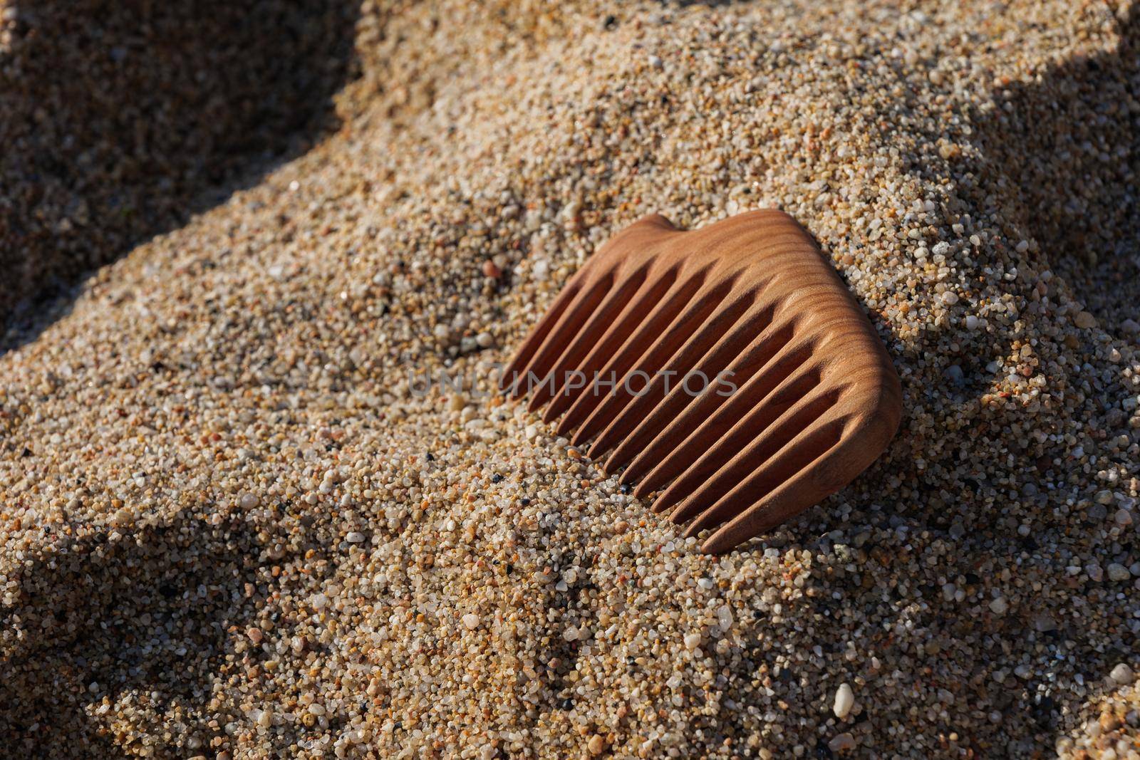 Handmade wooden comb on sand at the beach. Used for head massage and combing. Hair care concept. by apavlin