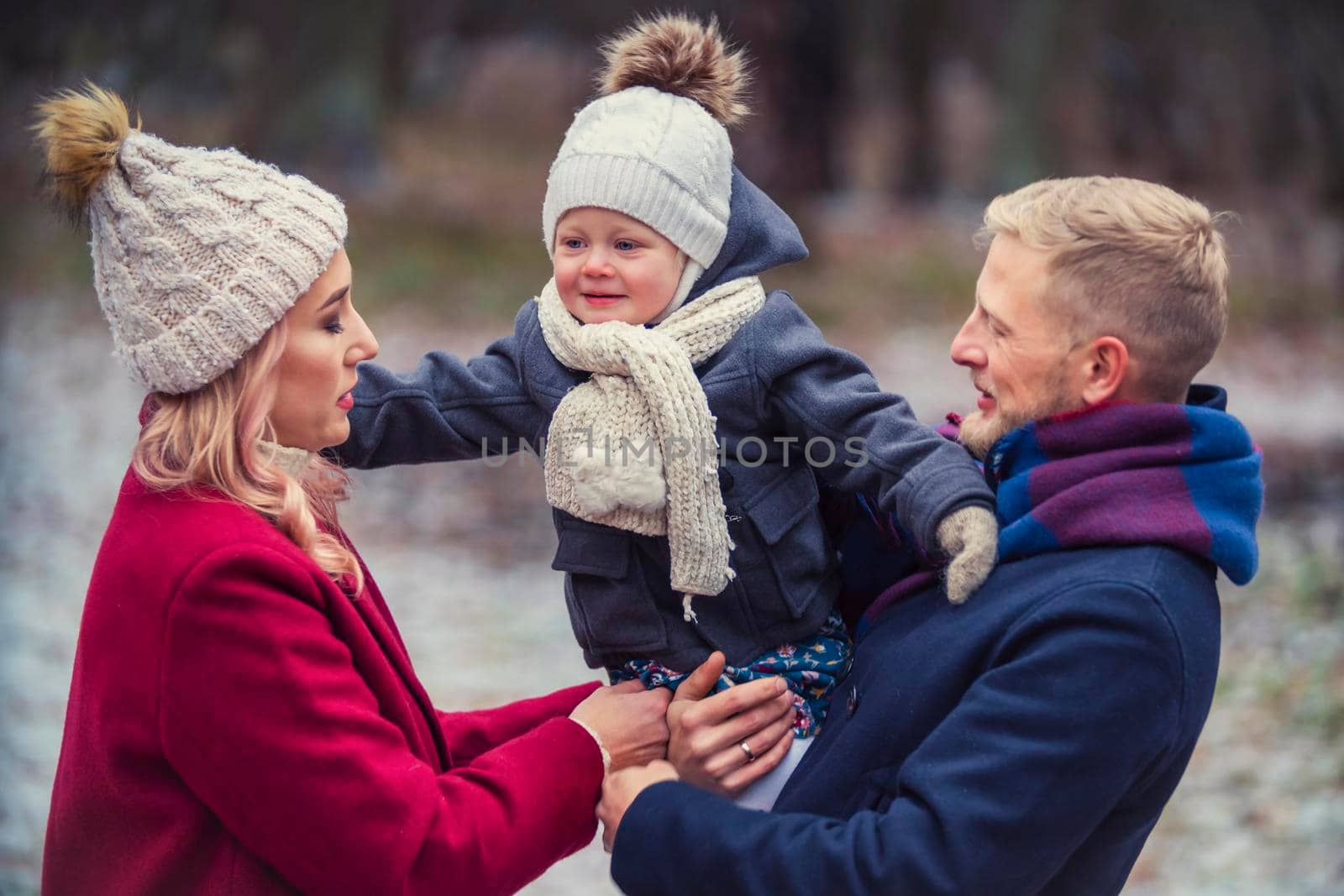 young family with a baby in their arms are walking in the park in winter