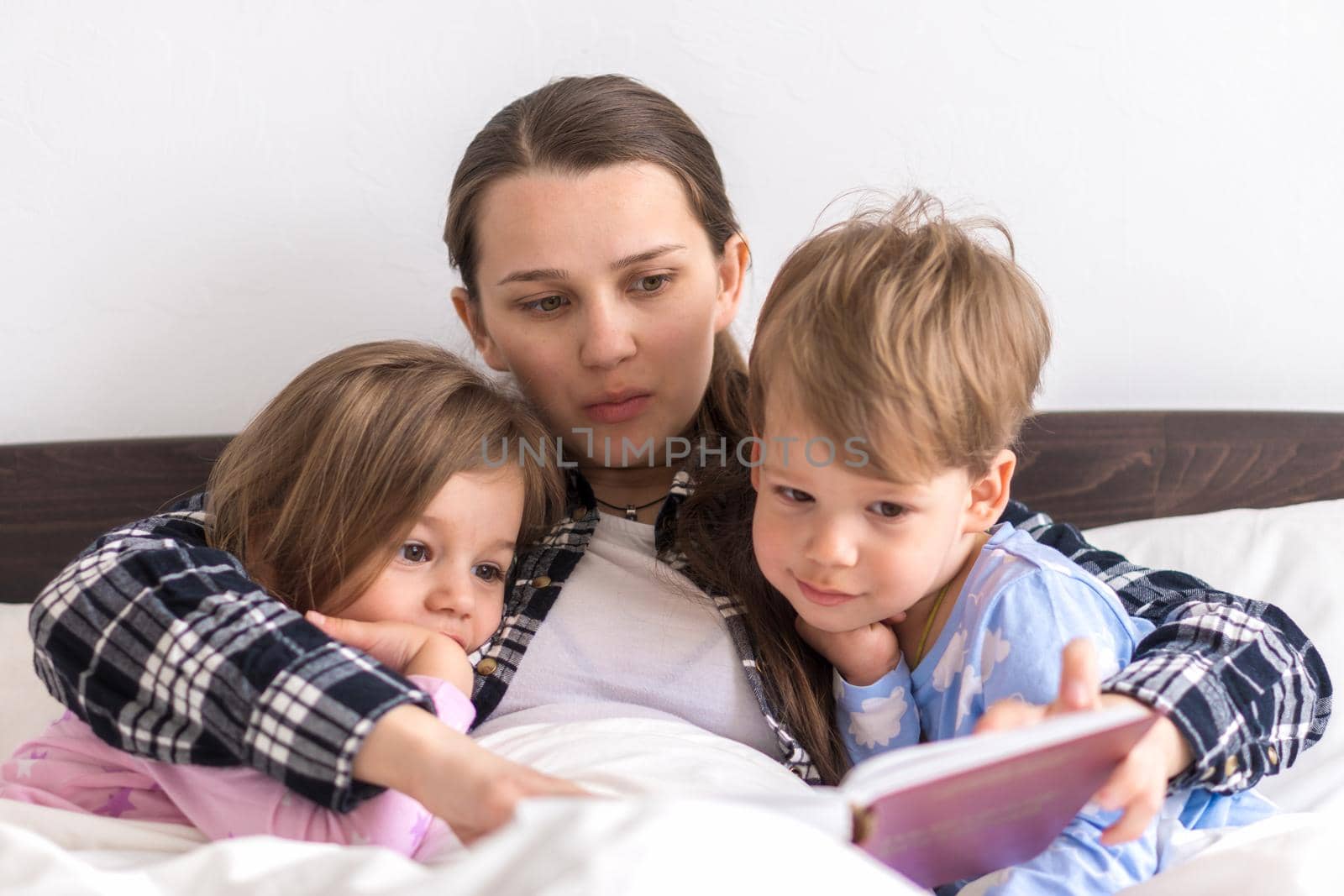 happy family. Close up loving mother lying with daughter son two kids pajamas in bed children reading interesting storybook, preschool smiling kid girl enjoy fairytale before go to sleep good pastime.
