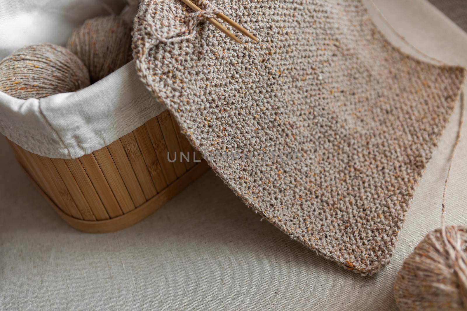 Close-up of knitted texture. Handmade wool scarf of sand color and basket with yarn balls. Selective focus