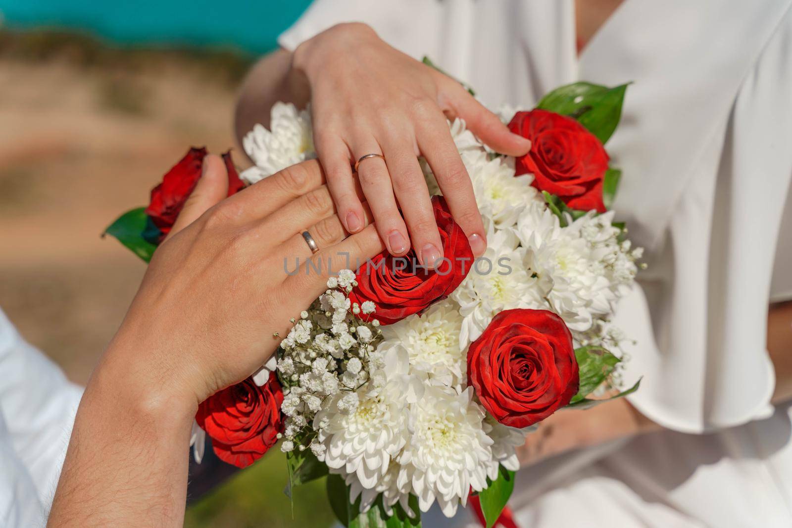 Hands of the groom and the bride with wedding rings on top of the bride's bouquet by Matiunina
