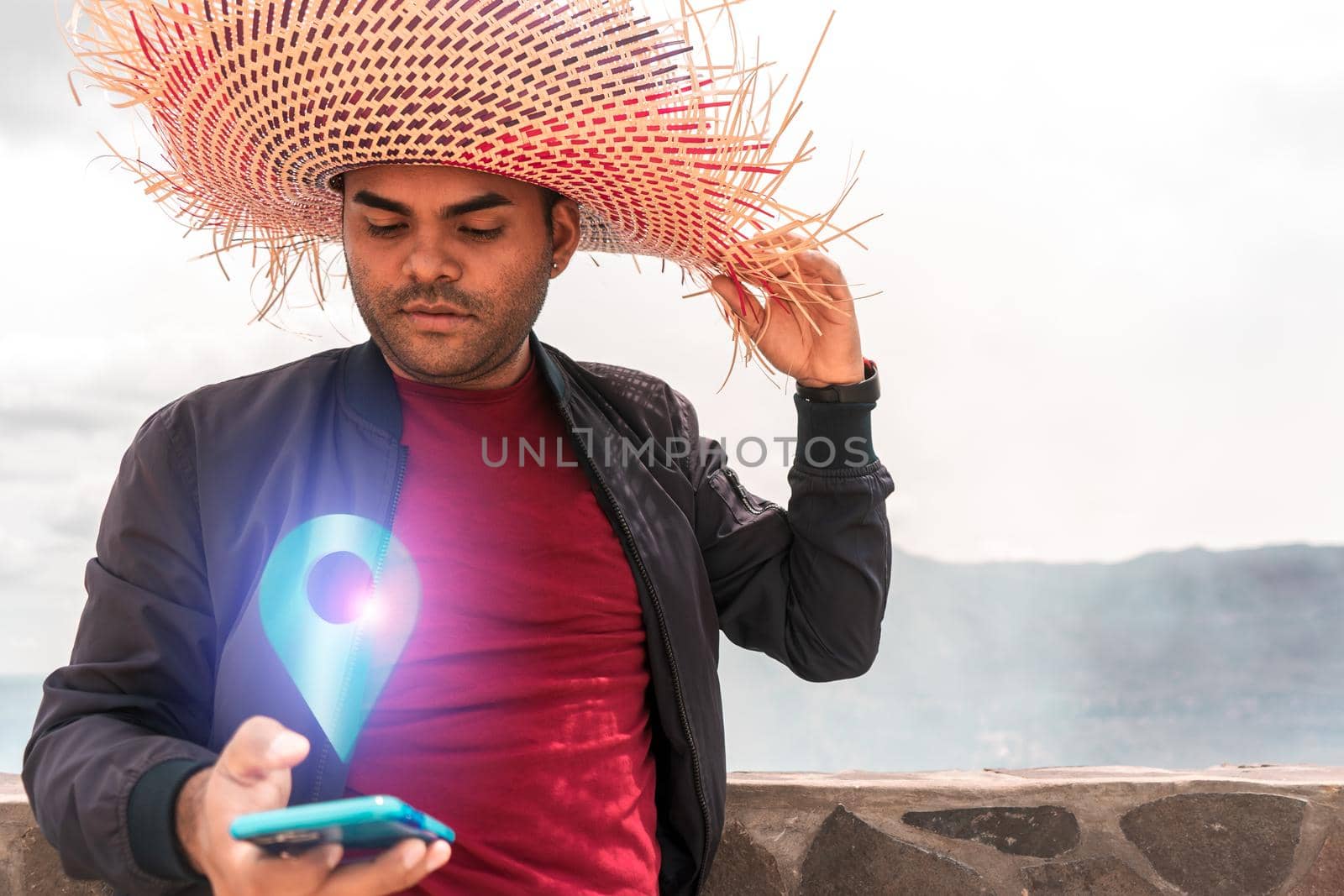 Latin man with striking hat searching for a location on his cell phone during an adventure trip in a volcano by cfalvarez