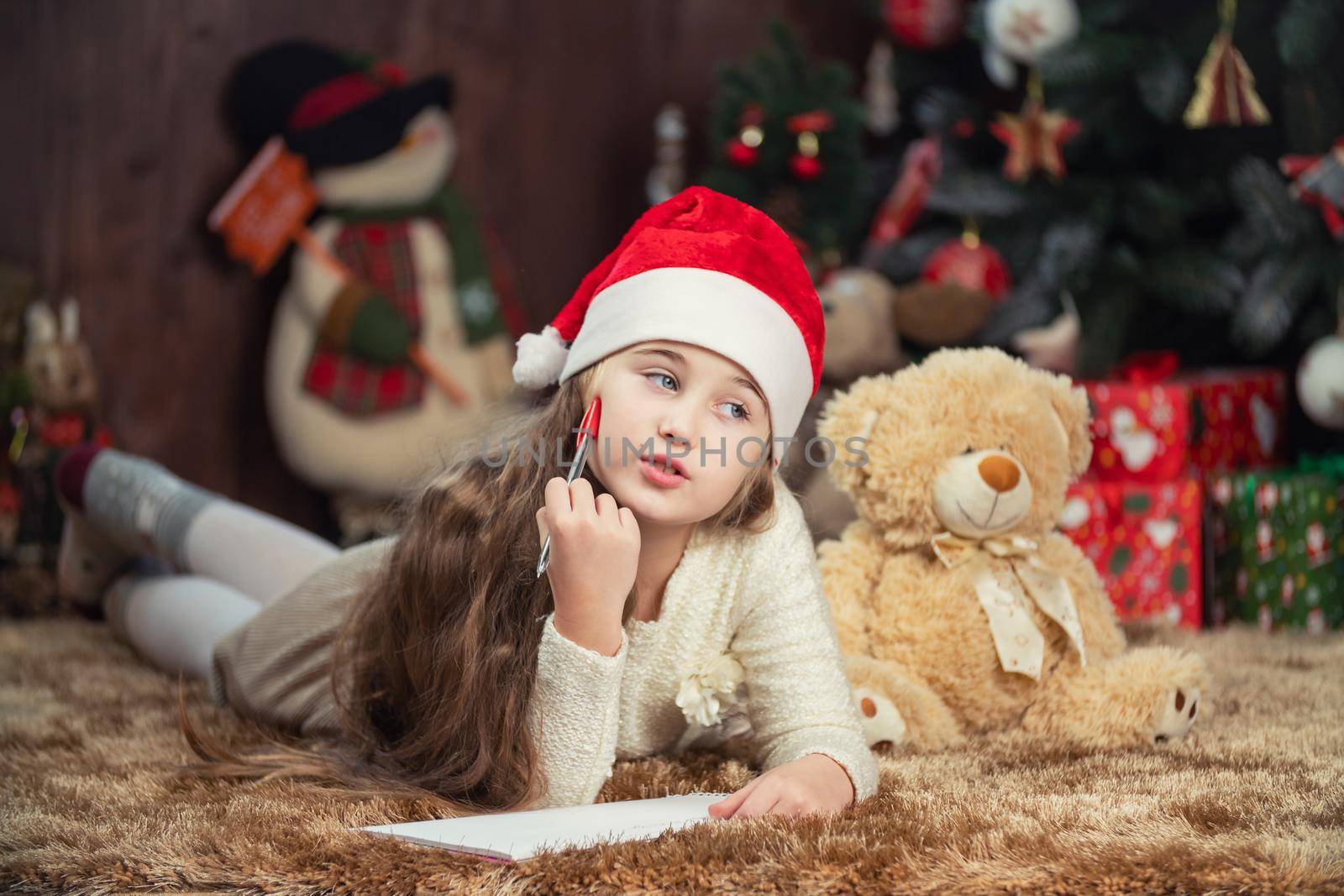 girl writing a letter to santa claus on the background of a decorated christmas tree