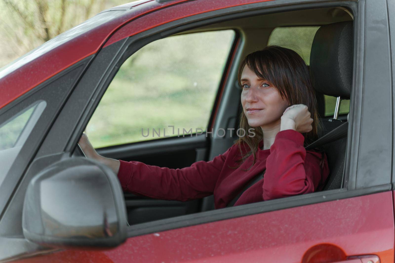 Dark-haired smiling girl in a burgundy sweatshirt driving a teracotta car