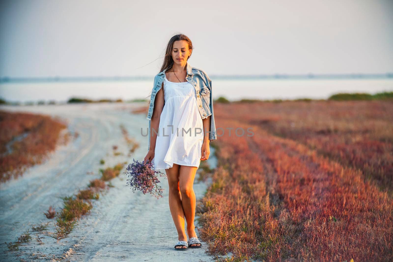 Woman with a bouquet of flowers walking on the road against the background of the sea