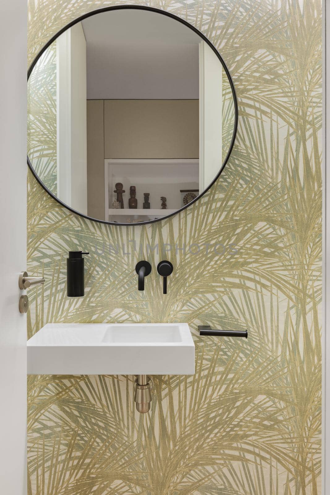 Bathroom with wallpaper with plant leaves texture, small wash basin and round mirror. Minimalist interior. by apavlin
