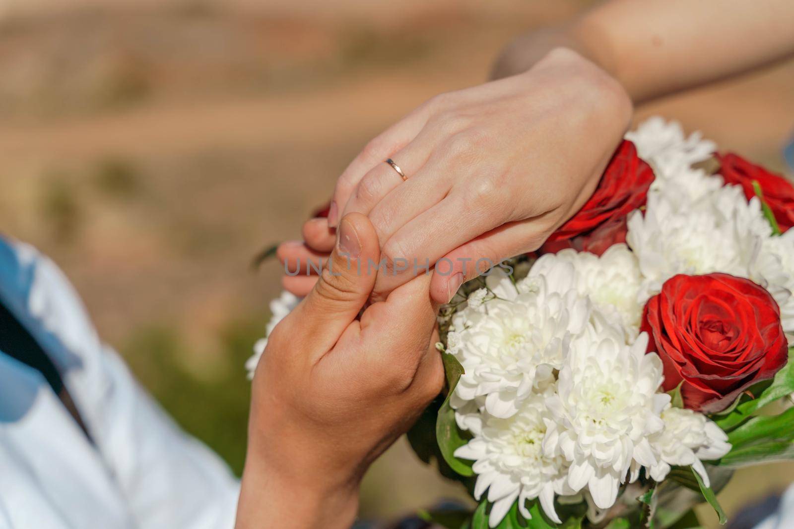 Hands of the groom and the bride with wedding rings on top of the bride's bouquet by Matiunina