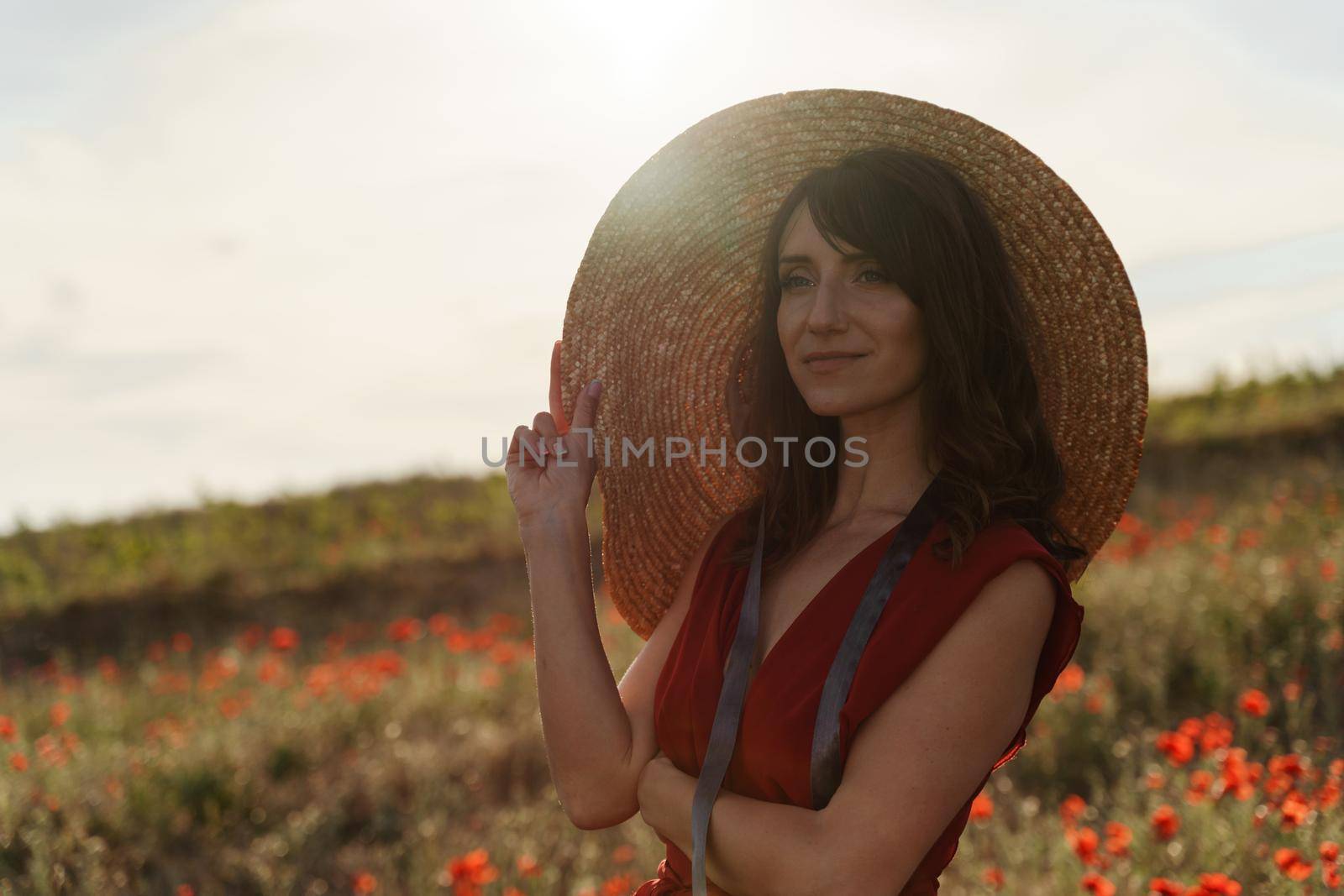 Young beautiful woman with closed eyes. In a white dress and a wreath of poppies on her head, she sits in a field of poppies at sunset with her hands folded under her chin
