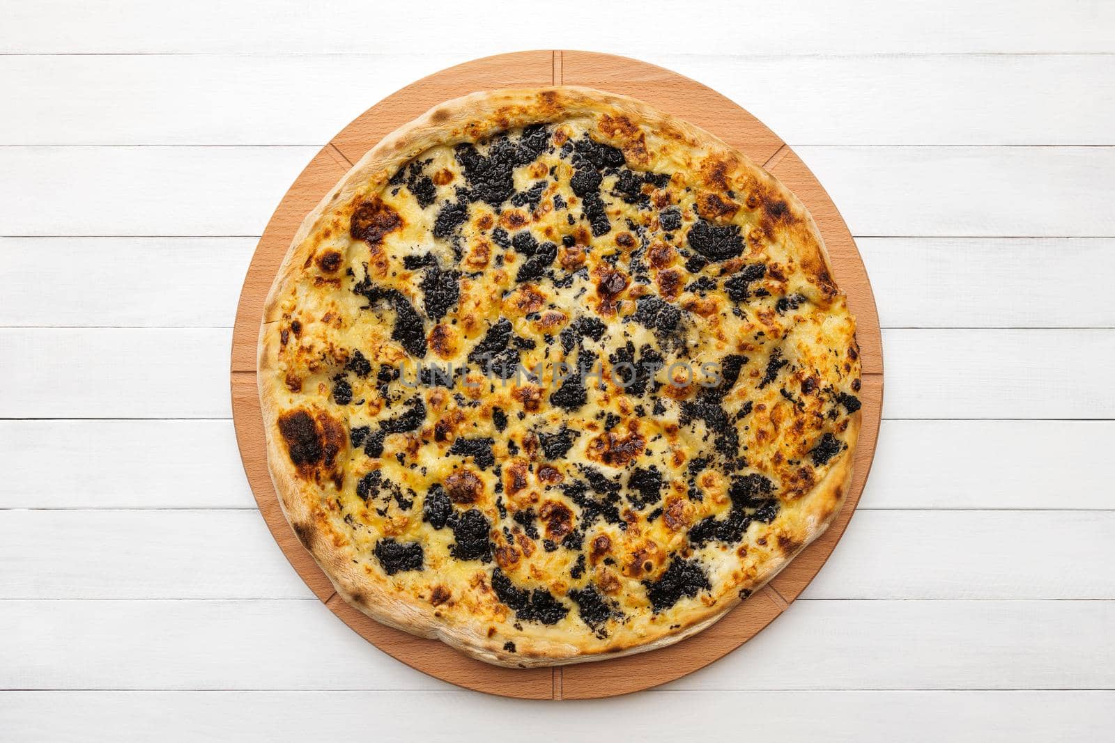 Whole round pizza topped with truffles and cheese on wooden plate. Top view on white board background by apavlin