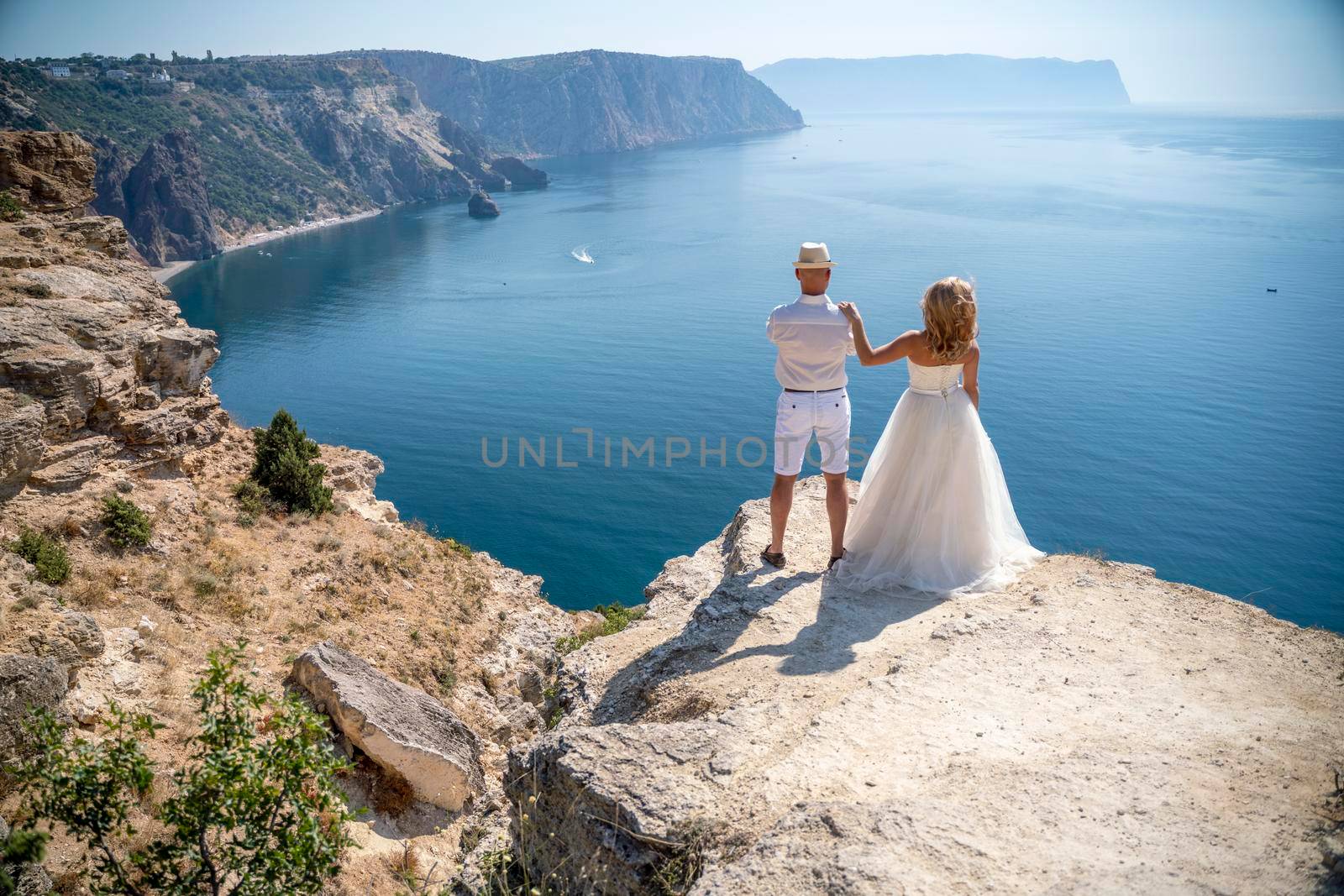 The newlyweds are standing, the bride has put her hand on the groom's shoulder, and look at the beautiful seascape Fiolent. The bride in a wedding dress, the groom in a white shirt, shorts, hat.