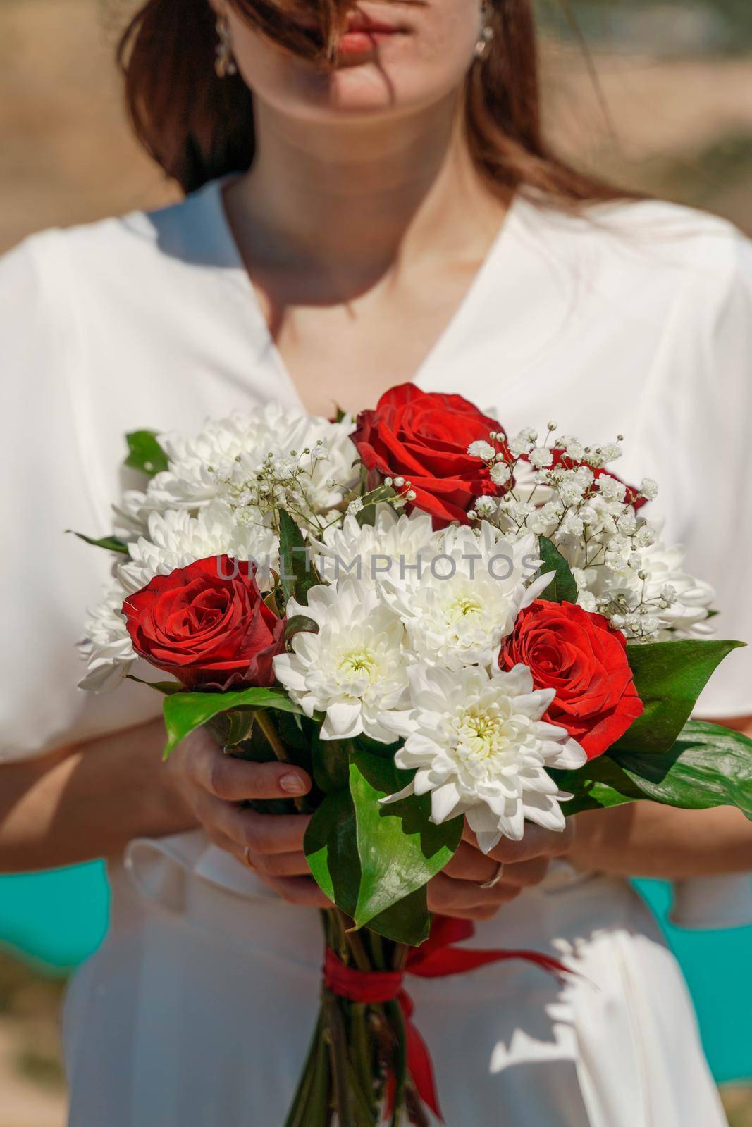 a bouquet of white chrysanthemums and red roses in the hands of the bride against the background of an azure lake