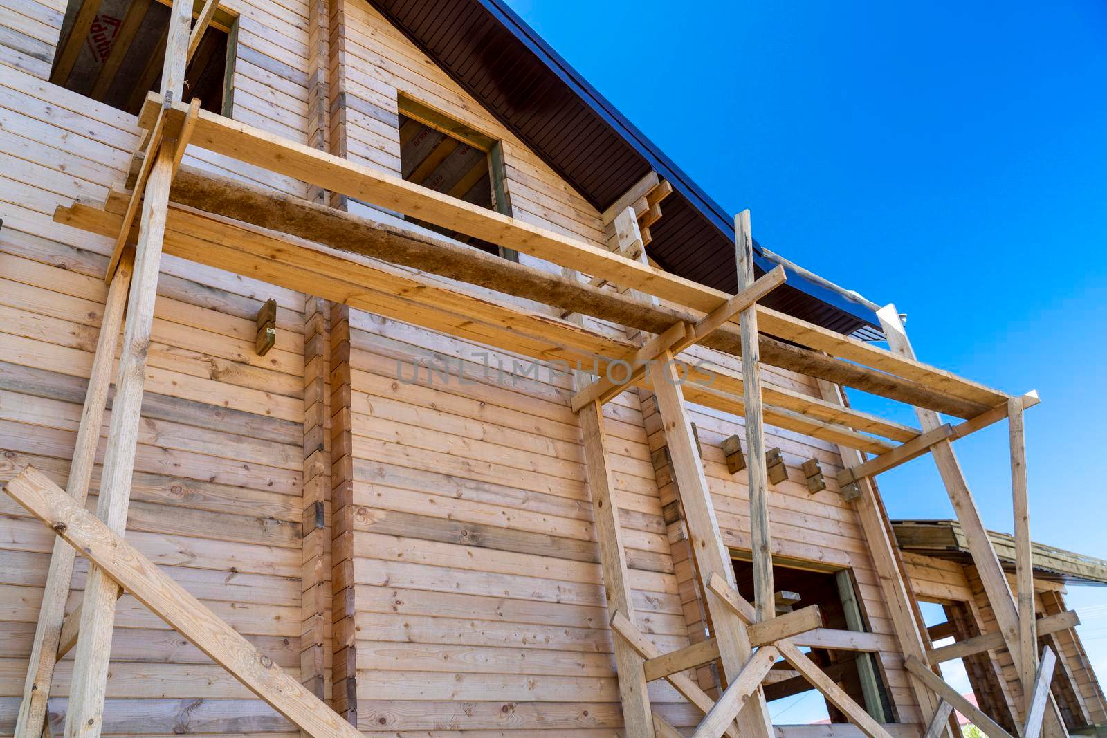 The house with a wooden structure is being built surrounded by scaffolding, blue sky. by Matiunina