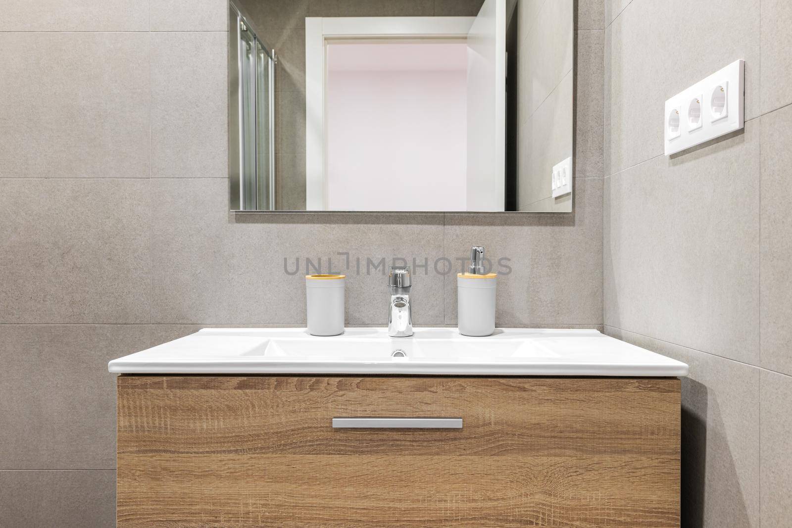 Close-up of white sink with modern wooden base and mirror in refurbished bathroom
