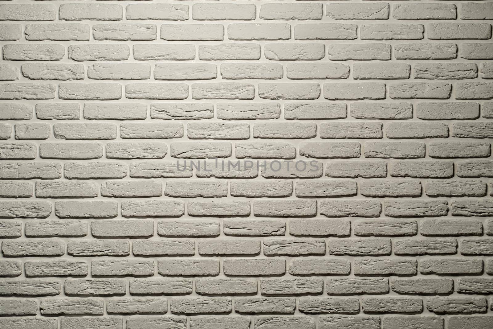 White brick wall of a warm shade lit from above by a lamp. White brick wall, perfect as a background, square photograph. The brick background is white with a warm shade