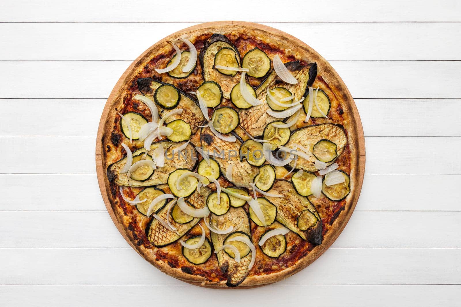 Whole vegetarian pizza topped with grilled eggplant, zucchini and onion, on wooden plate. Top view on white board background. Copy space.