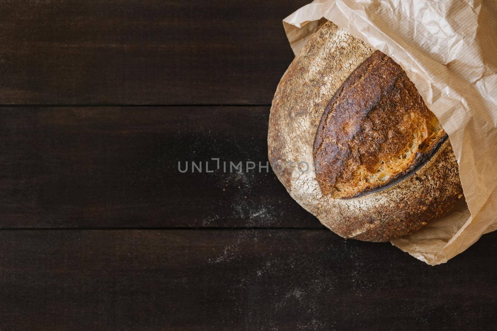 Homemade wheat bread on dark wooden background with particles of flour. Top view of crispy baked bread surface texture.