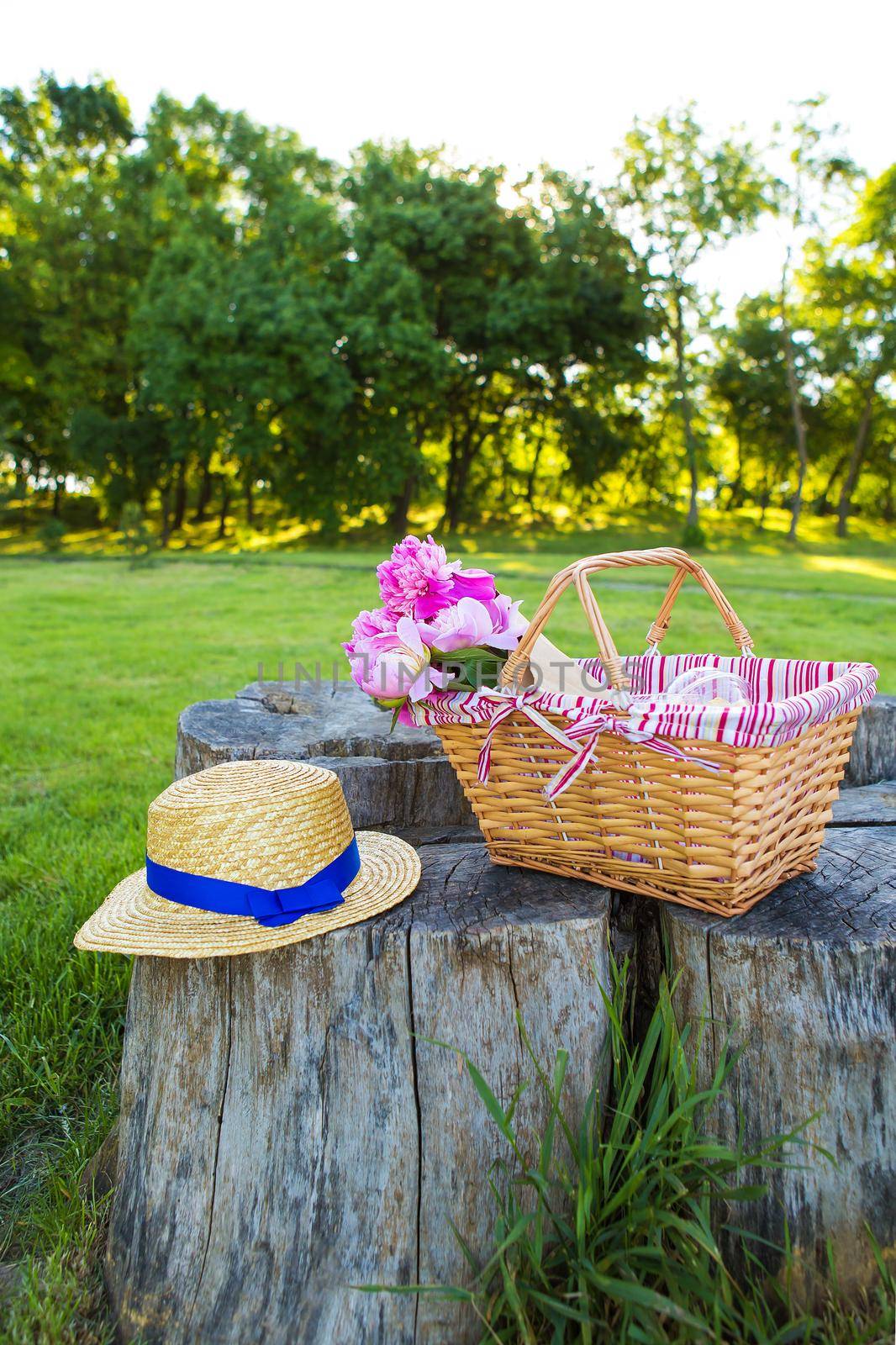 Beautiful straw hat and flowers in a basket stand on a wooden stump