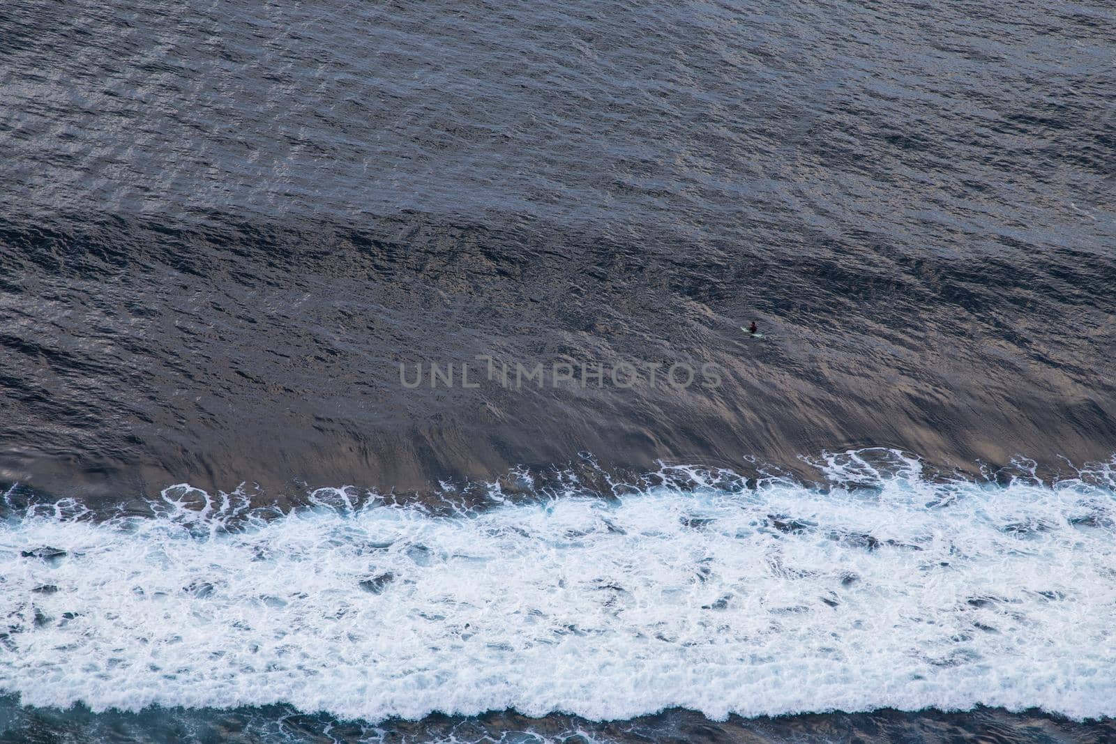 Aerial view of ocean with wave and lonely surfer in blue water. Atlantic ocean.