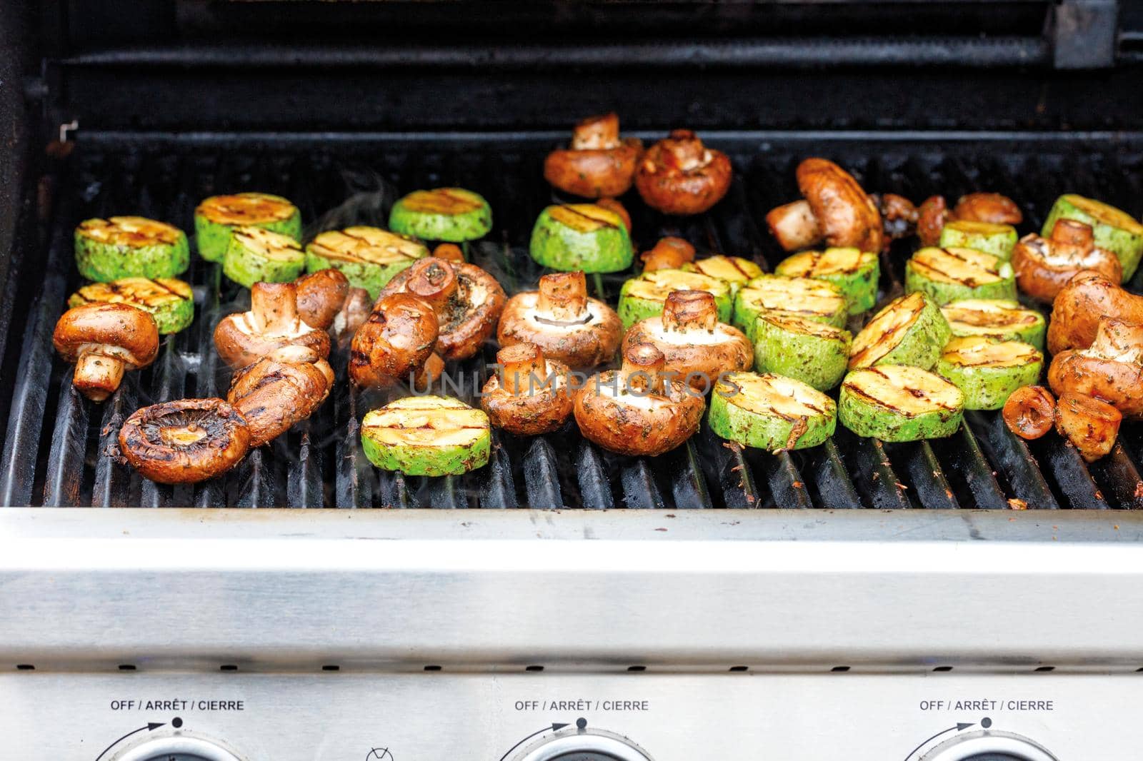 Delicious champignons and green zucchini are being cooked on a gas grill, close-up, selective focus. by Sergii