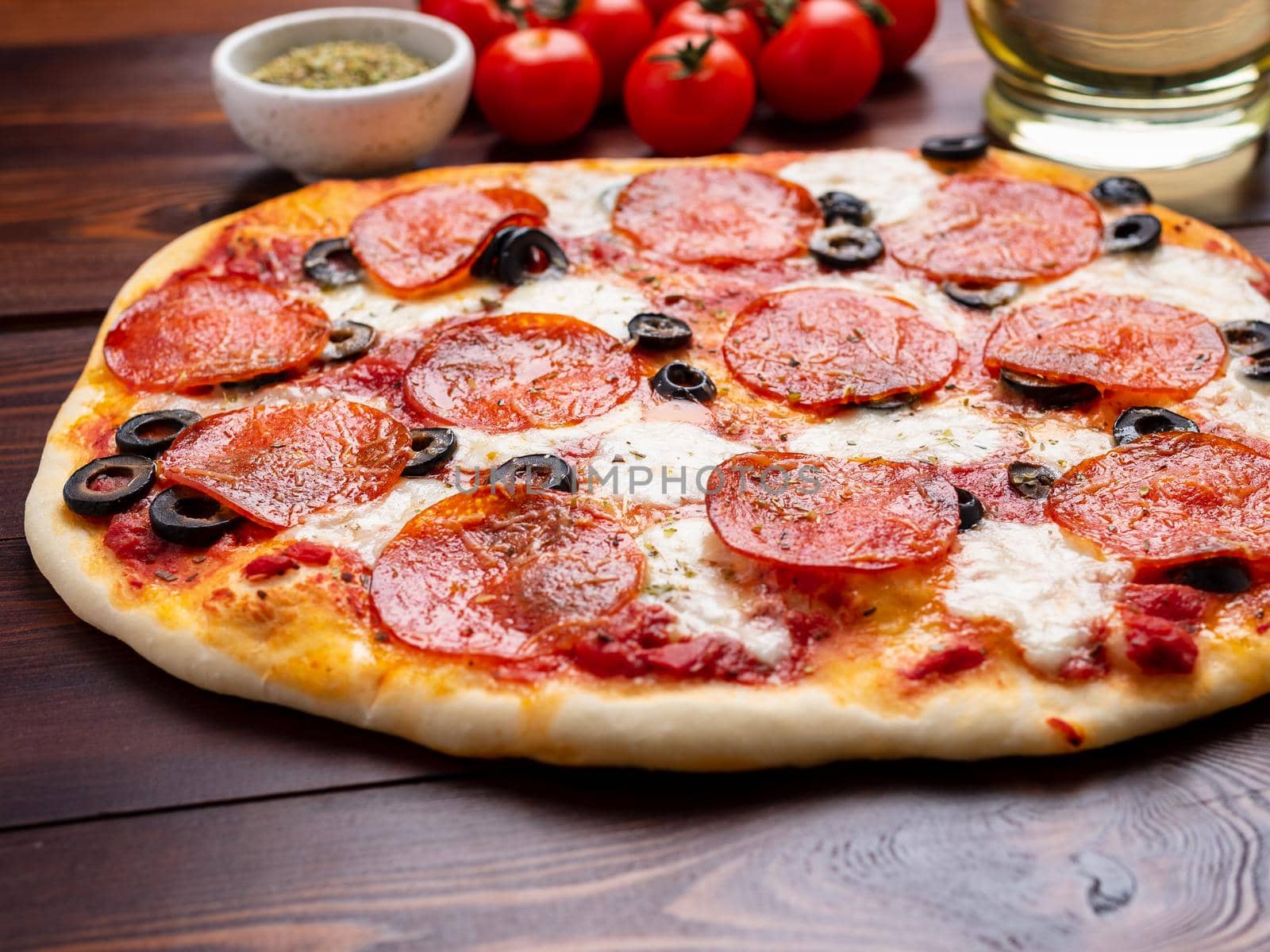 hot homemade Italian pepperoni pizza with salami, mozzarella and olives on a dark brown wooden table.