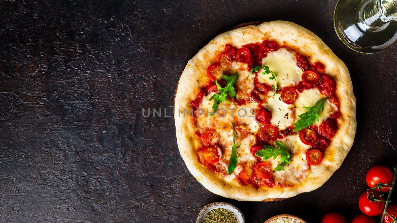 hot homemade Italian pizza margherita with mozzarella and tomatoes on dark brown stone table, top view, copy space.