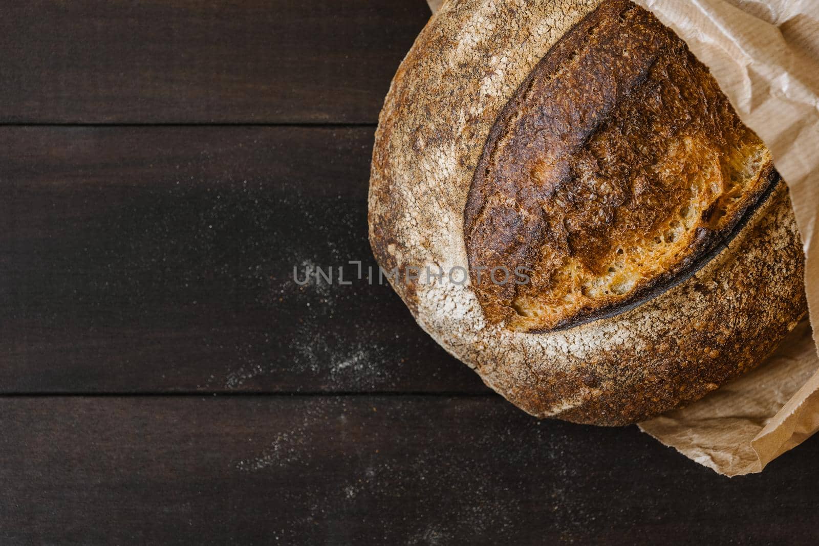 Close-up of homemade wheat bread on wooden table with flour particles around. Crispy baked bread surface texture. Flat lay, top view, copy space concept
