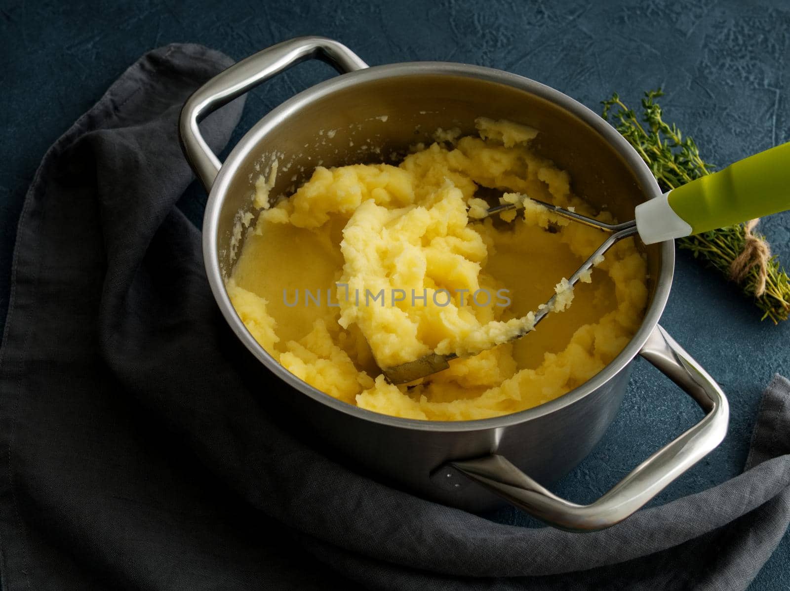 Mashed potatoes in bowl on a dark stone blue table, rosemary, napkin, side view, close up