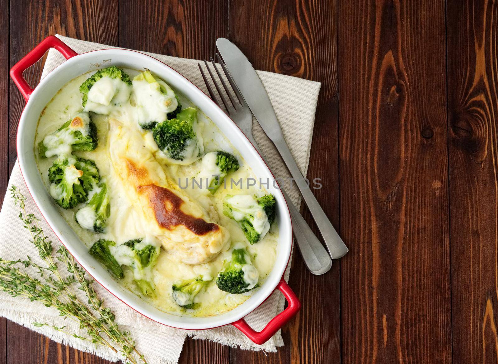 Chicken fillet baked with broccoli in bechamel sauce on a dark wooden table. Healthy food, clean eating, top view, copy space